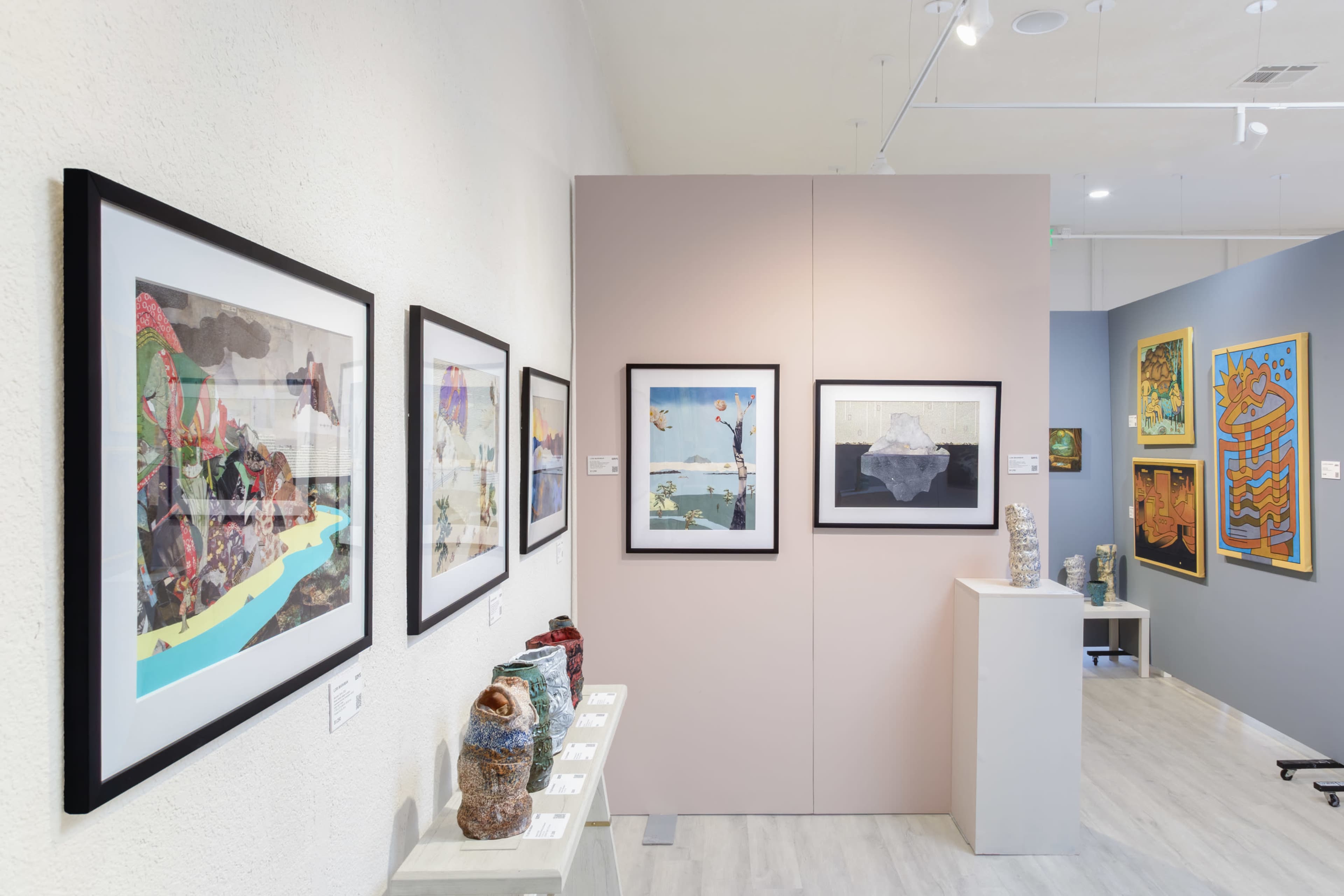 The image shows an art gallery featuring a display of framed artworks on the walls and various sculptures on display pedestals.