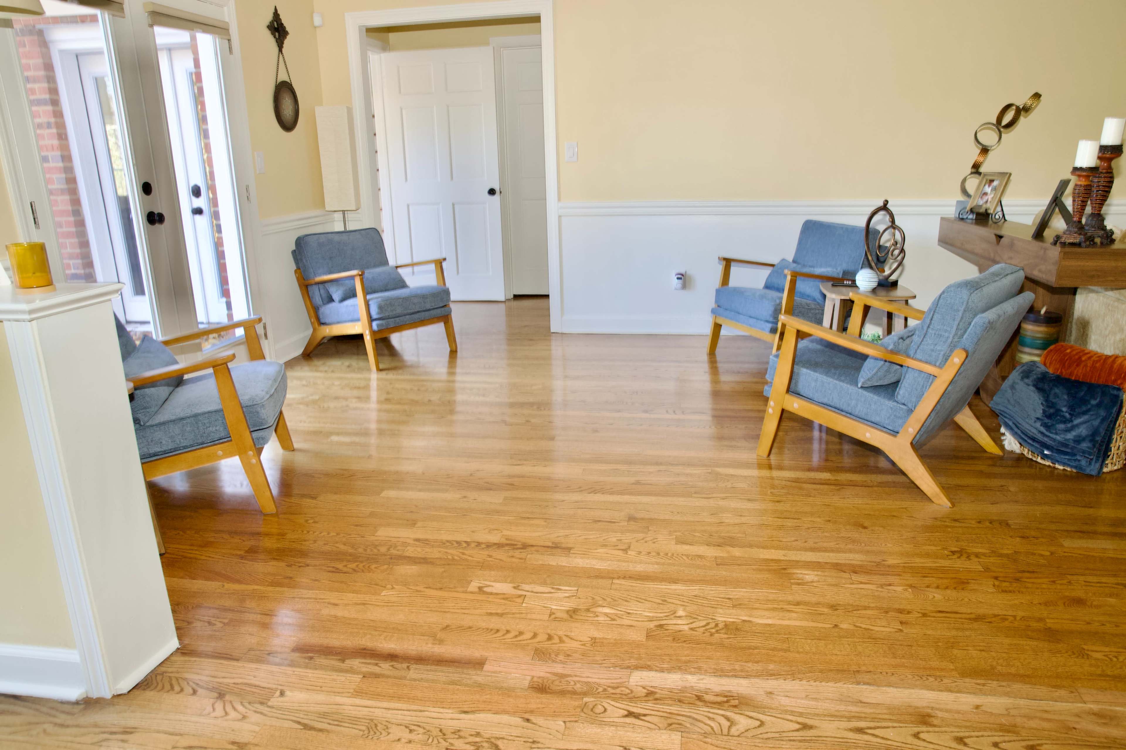 The image shows a light-filled room with four blue chairs arranged around a wooden coffee table on polished hardwood flooring.