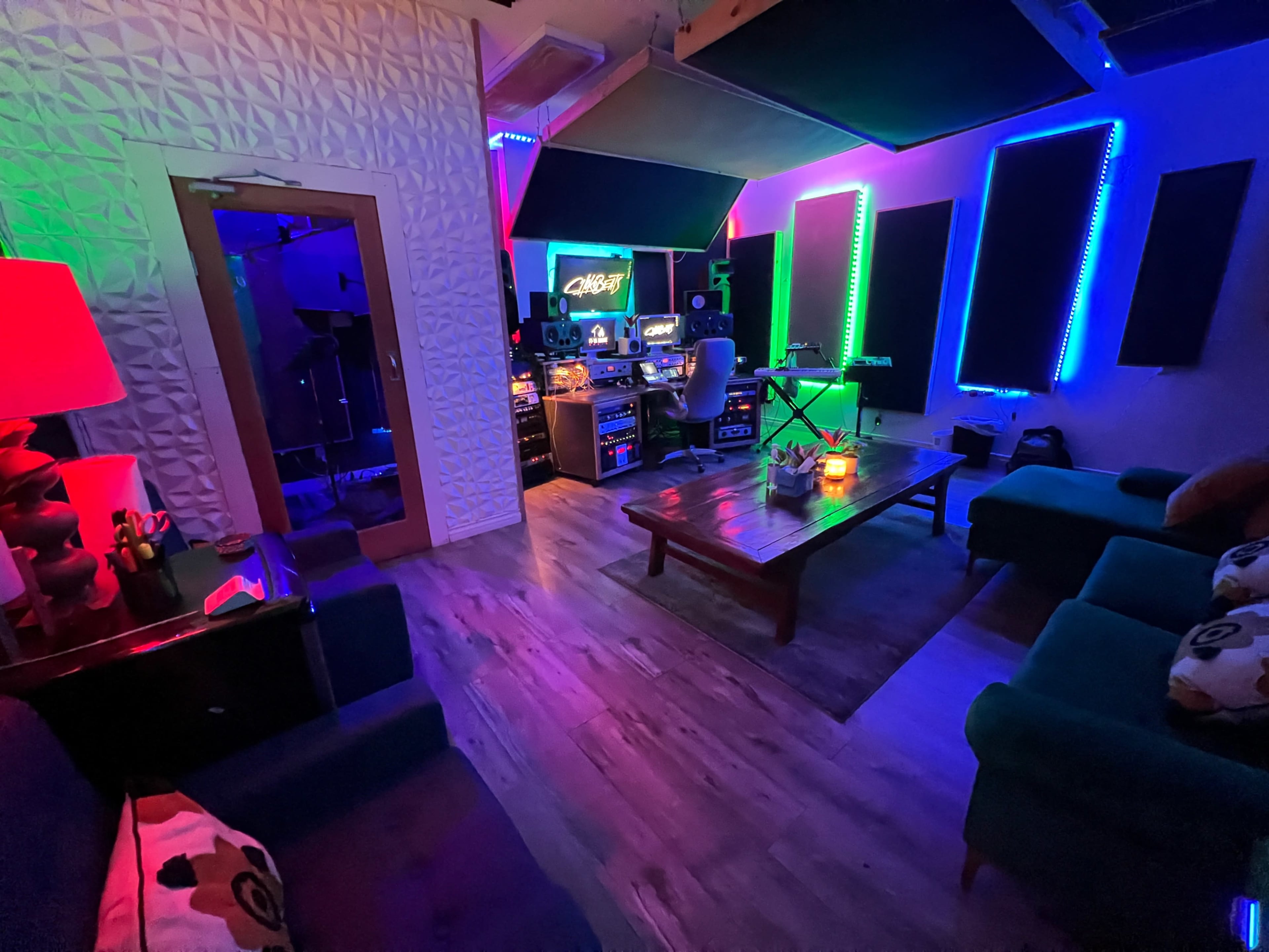 The image shows a music studio with colorful LED lighting, a mixing desk, and various musical equipment, surrounded by a seating area.