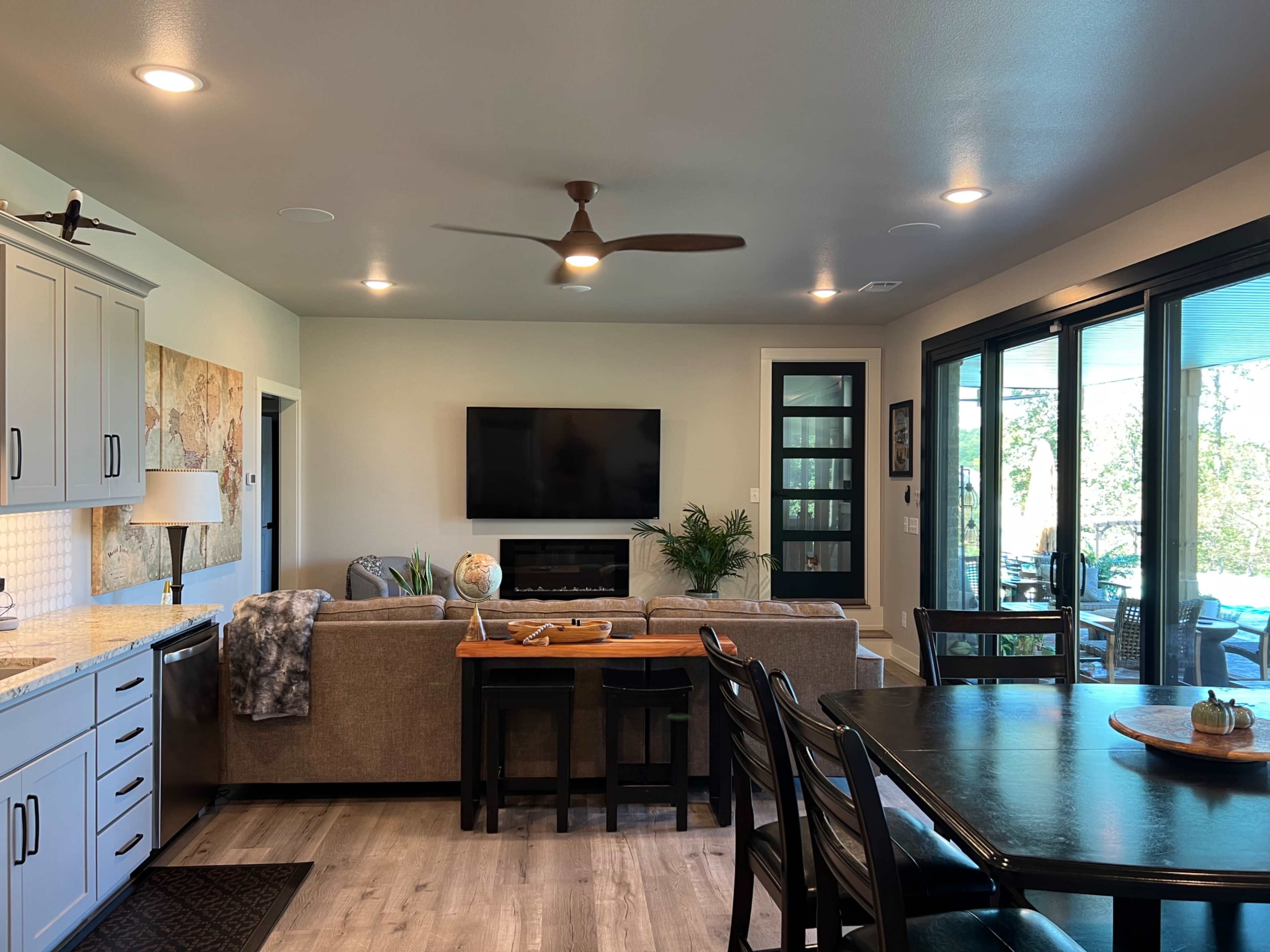 A modern living space features a sofa, coffee table, and wall-mounted television, with large windows providing a view of the outdoors.