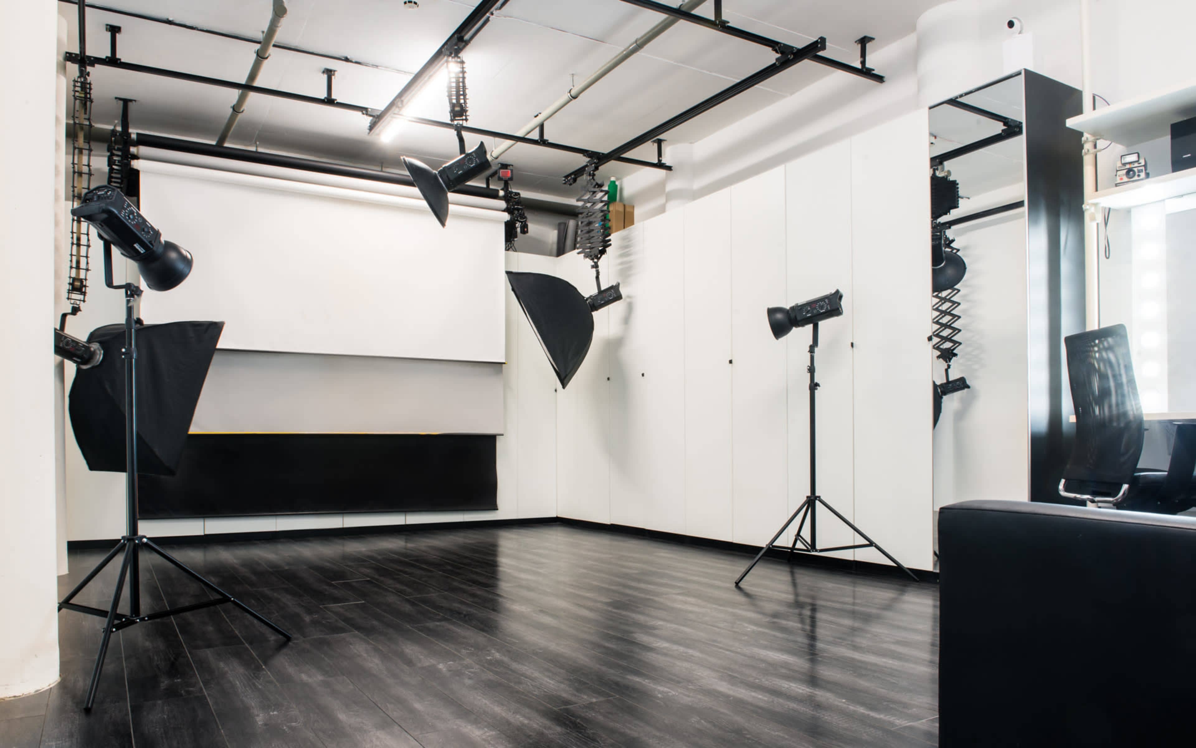 The image shows a photography studio equipped with black and white walls, multiple light sources on stands, and a backdrop area.