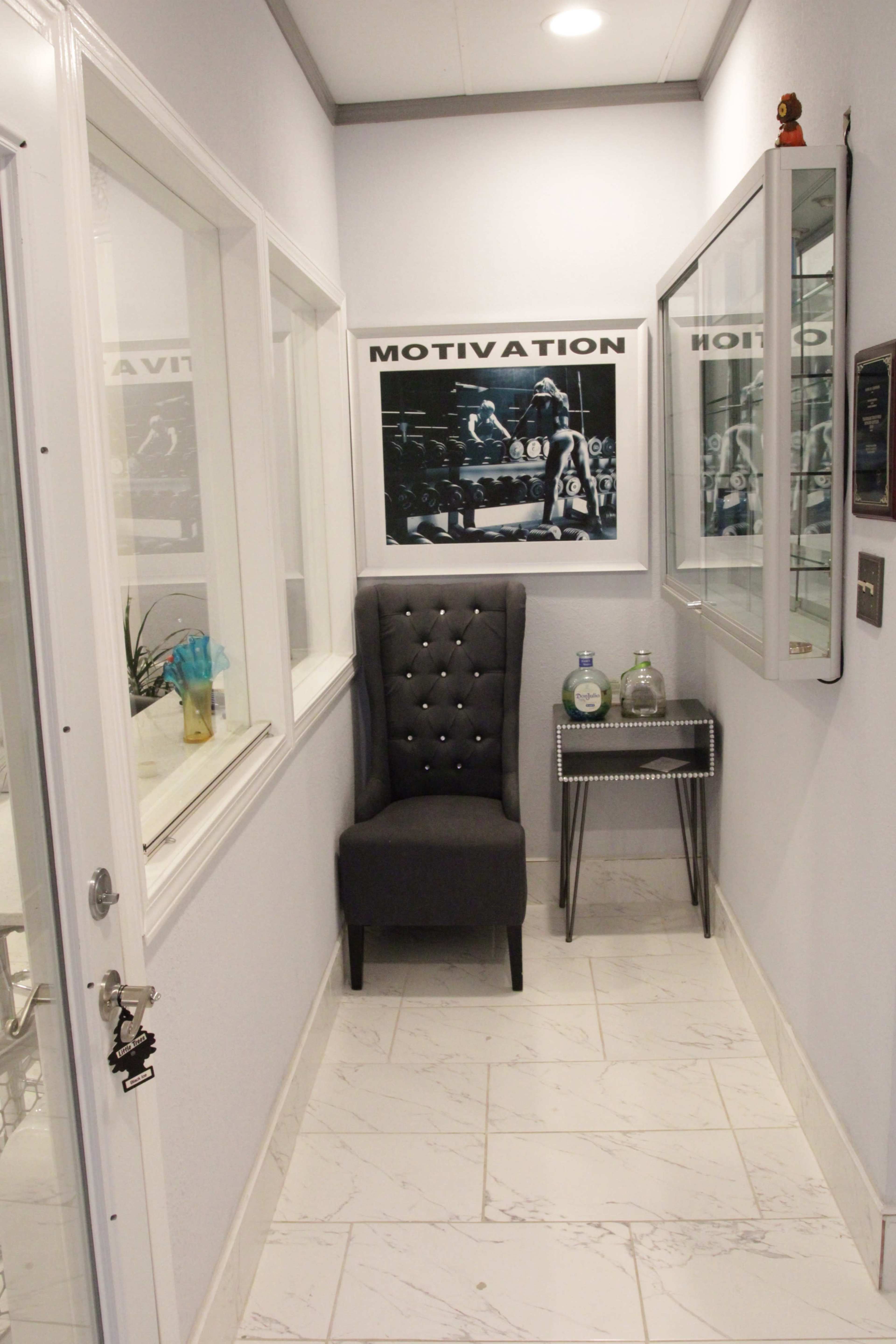 A narrow hallway featuring a plush gray chair, a decorative side table, and framed motivational artwork on the walls.