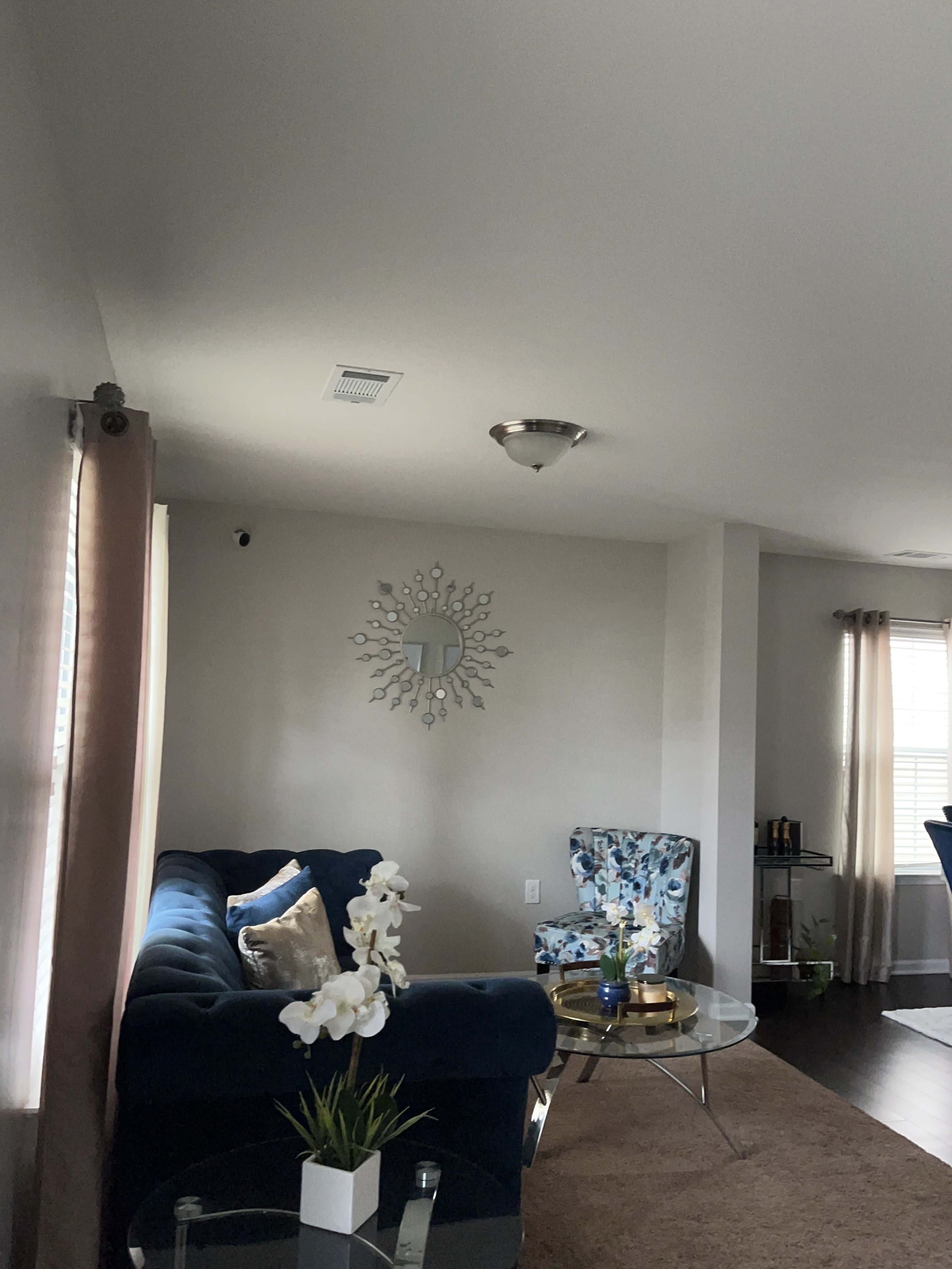 A living room with a blue sofa, a patterned chair, a round mirror on the wall, and a coffee table with flowers.