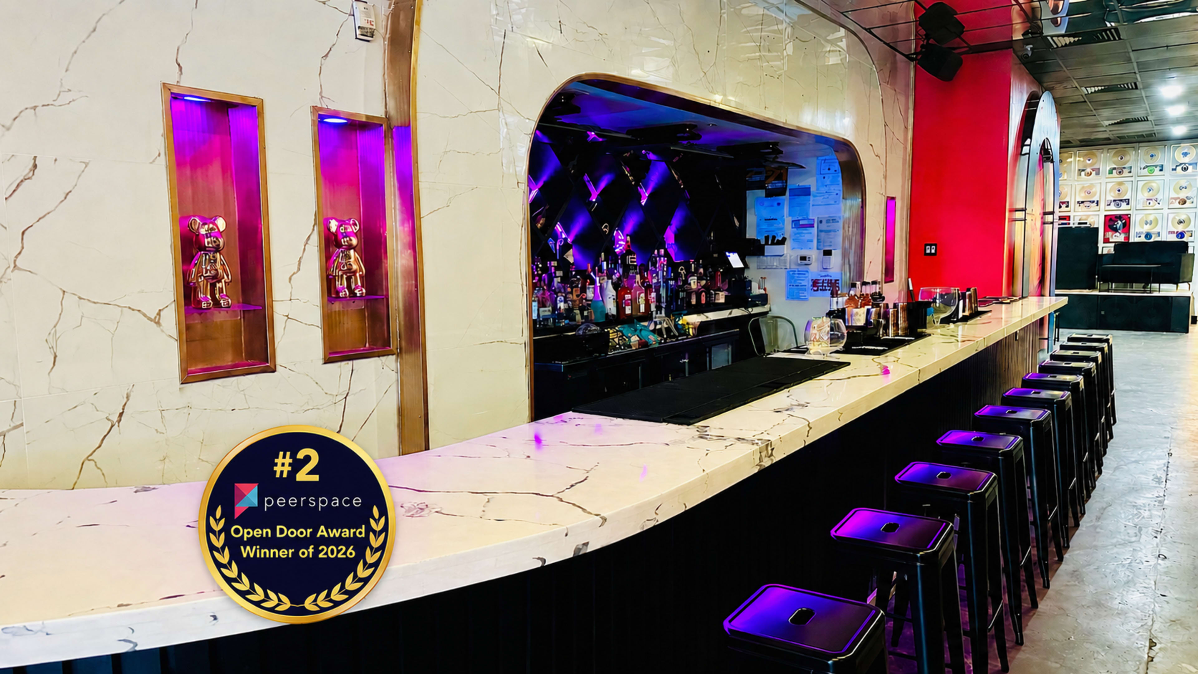 The image shows a modern bar with a sleek marble countertop, illuminated by purple lighting, and featuring decorative statues on the wall.