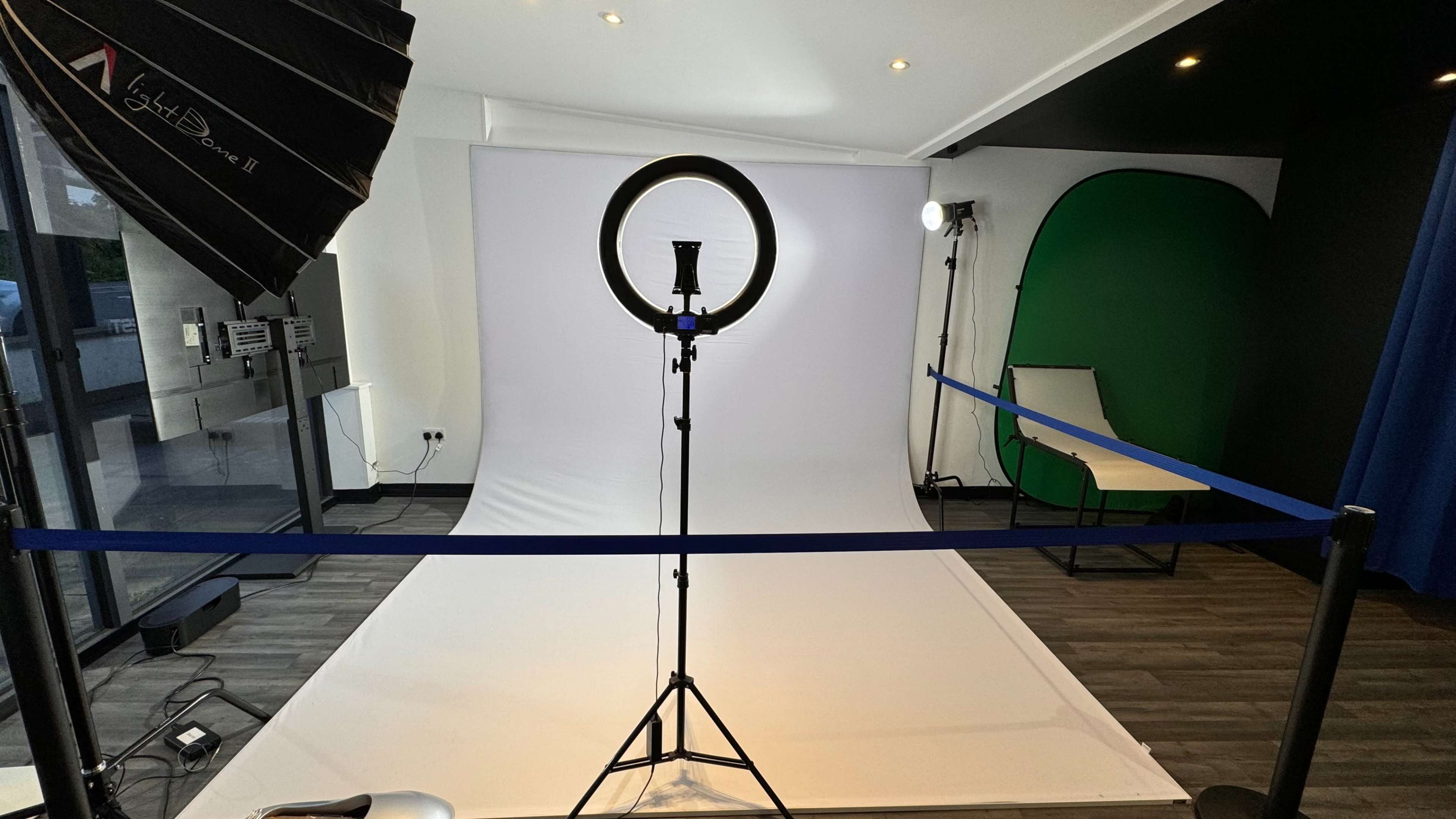 A photography studio setup features a white backdrop, a ring light on a stand, and various lighting equipment in a well-lit room.