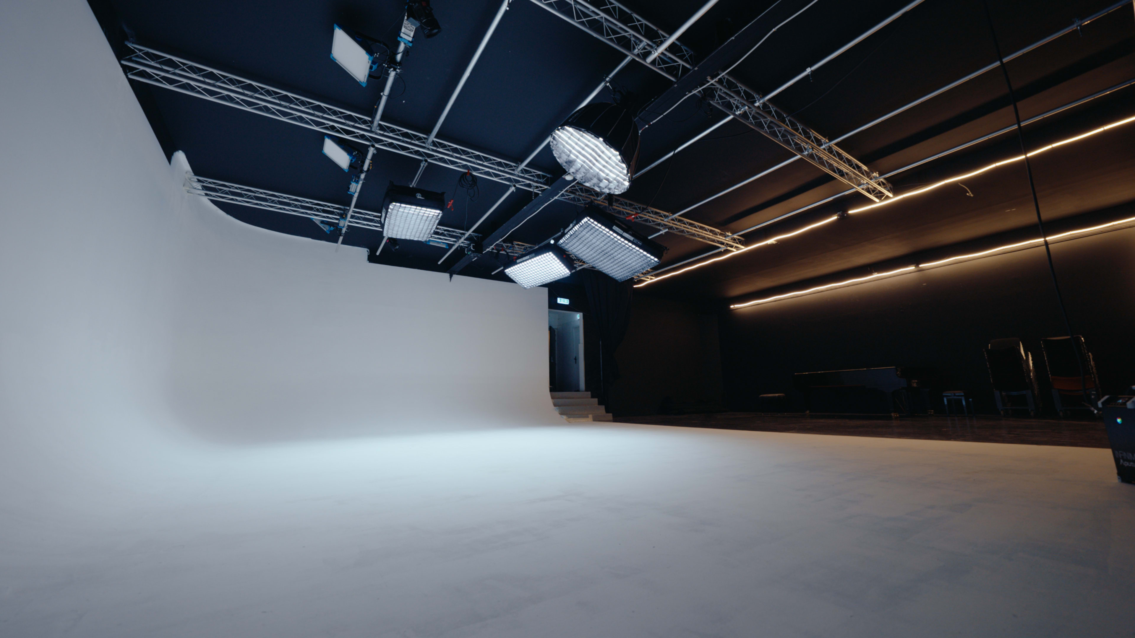 The image shows a large, empty studio space with a smooth white backdrop and multiple lighting setups overhead.