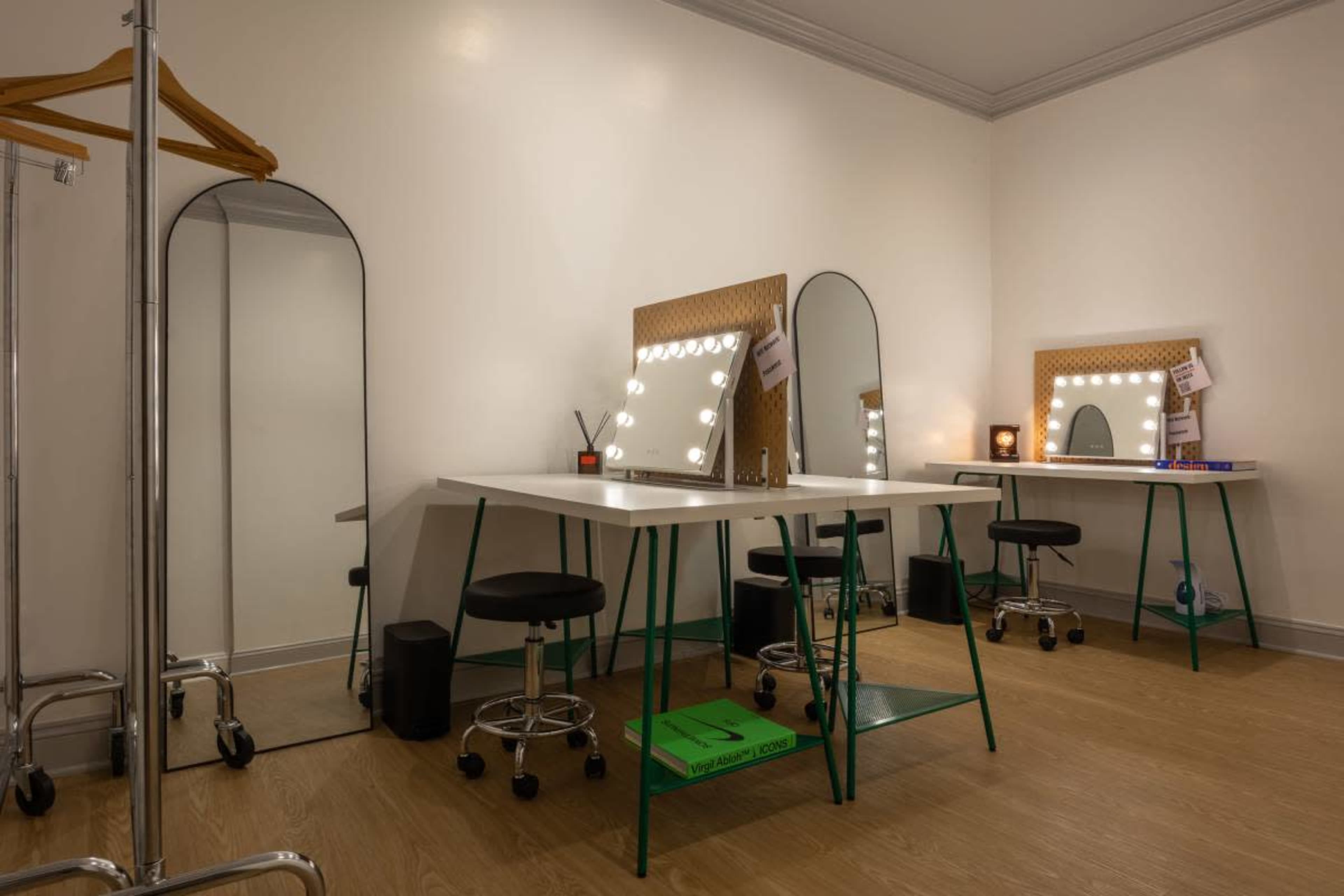 The image shows a bright and modern dressing room with two makeup tables featuring illuminated mirrors, stools, and a full-length mirror in the corner.