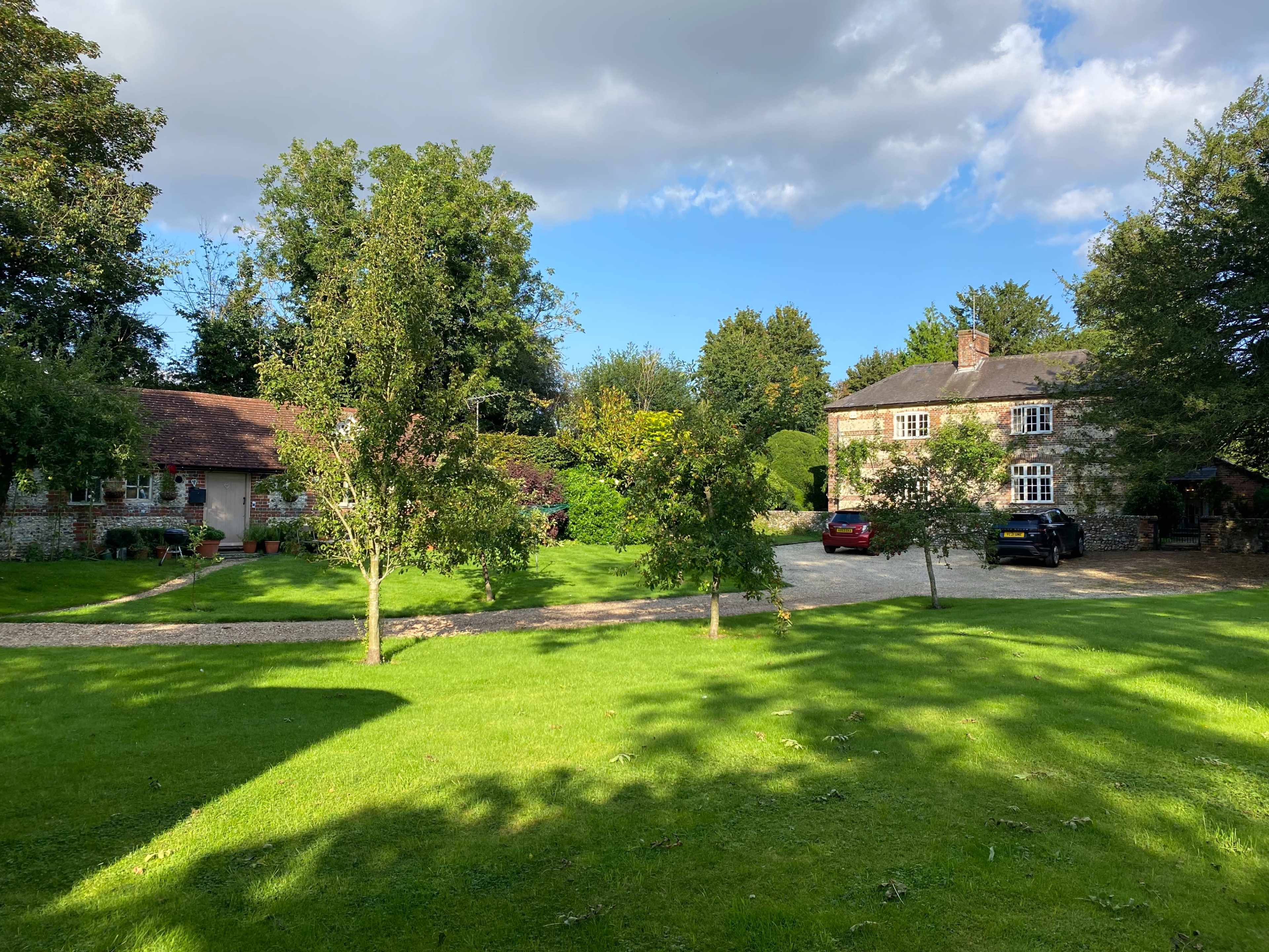 Two houses surrounded by a green lawn and trees under a partly cloudy sky.