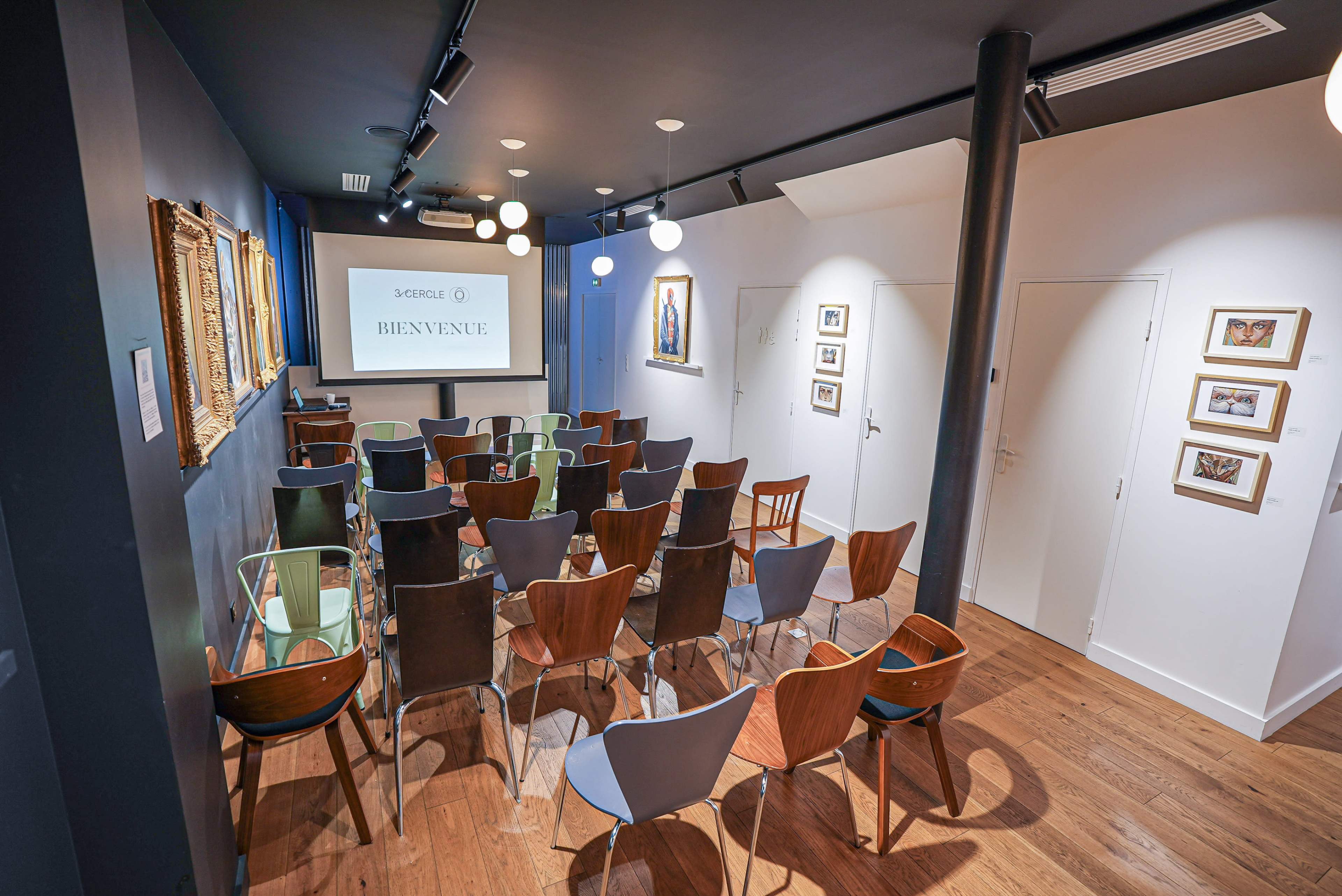 A small, modern seminar room features rows of chairs facing a projection screen, with walls adorned with framed artwork.