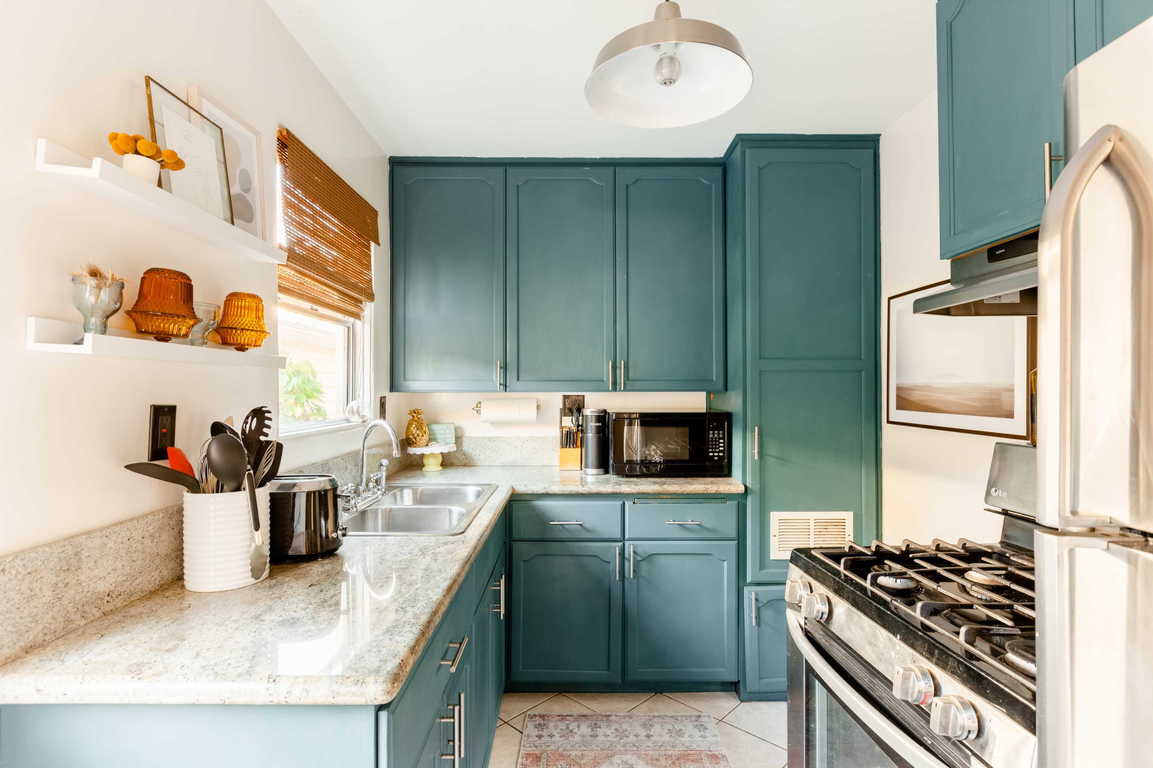 A small kitchen with teal cabinets, a granite countertop, a stove, and a microwave on the countertop.