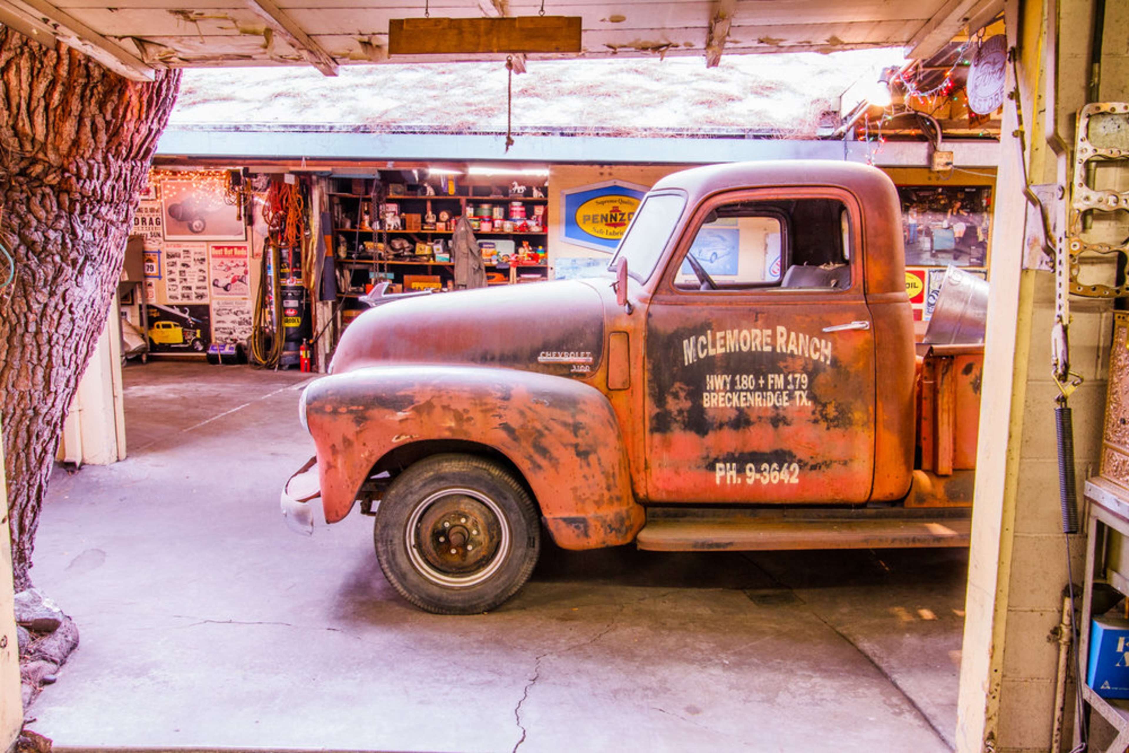A vintage, rust-covered pickup truck is parked in a garage filled with tools and equipment.