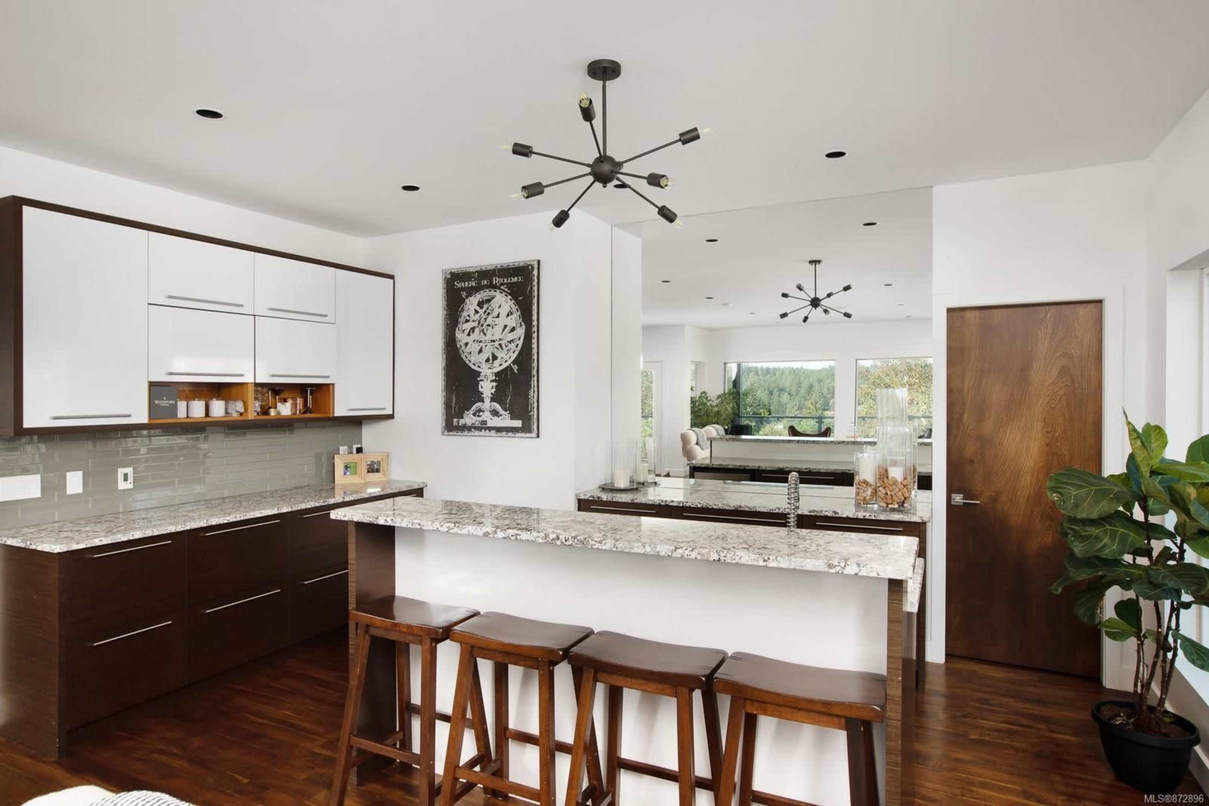 A modern kitchen with dark wood cabinets, a granite countertop, and a small dining area with bar stools.