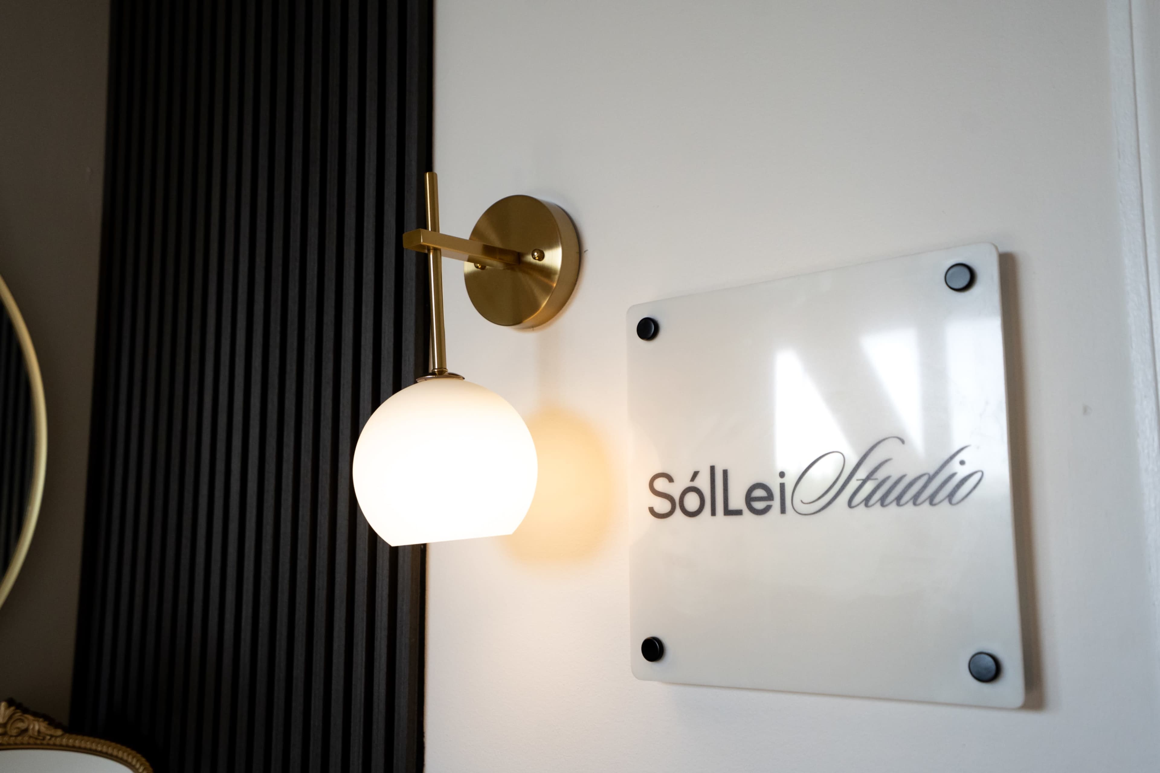 The image shows a wall-mounted light fixture next to an elegant sign that reads "SólLei Studio."