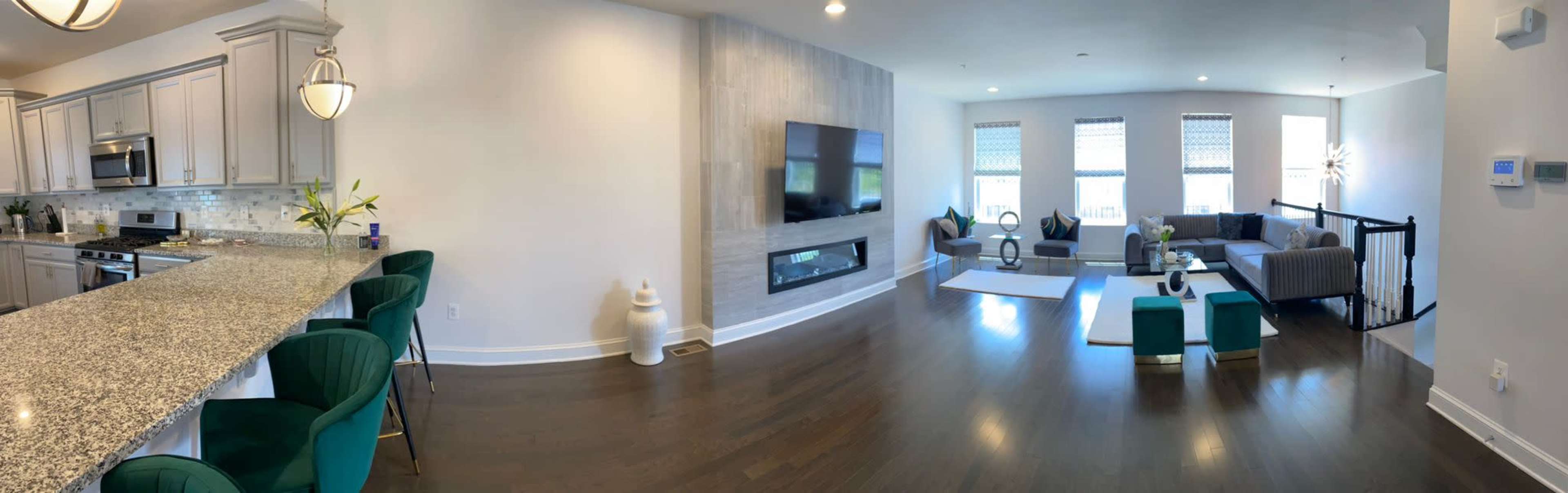 A modern open-concept living space with a kitchen featuring a granite countertop and bar seating, an entertainment area with a fireplace, and ample natural light from large windows.