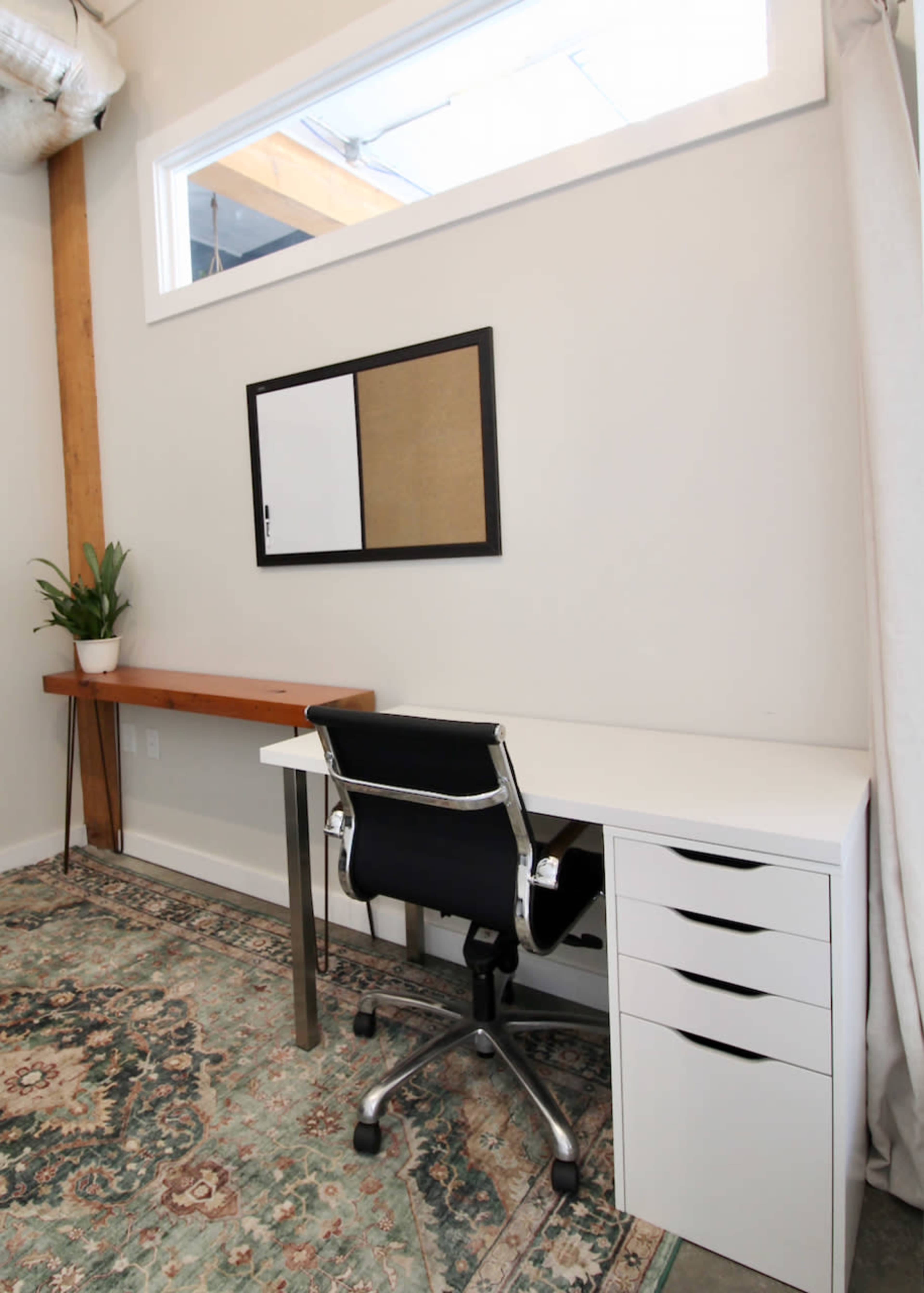 The image shows a modern workspace with a white desk, an ergonomic chair, and a wall-mounted mirror above the desk, accompanied by a decorative plant and a wooden shelf against the wall.