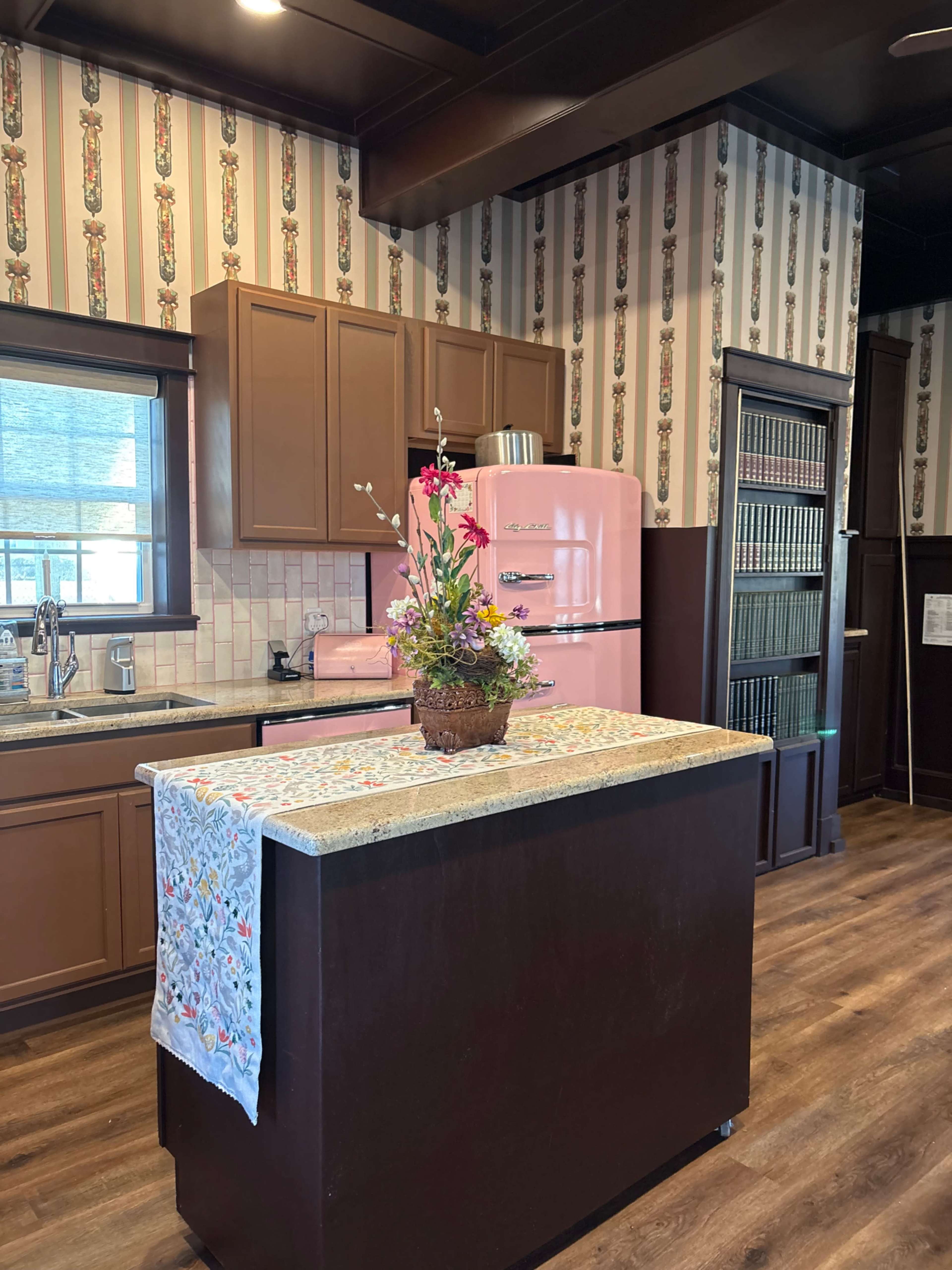 The kitchen features a pink retro refrigerator, brown cabinets, and a central island decorated with a floral arrangement.