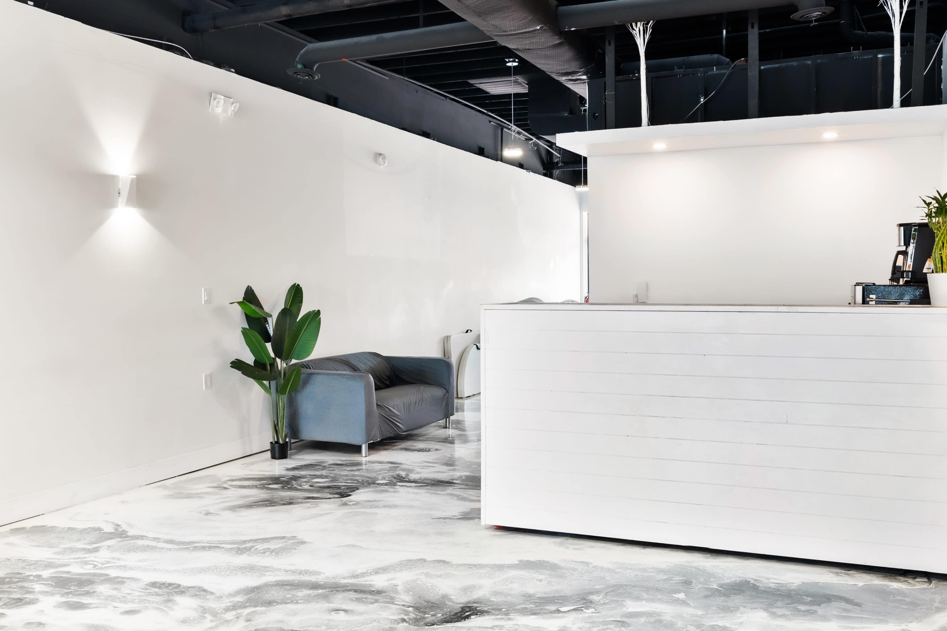 The image shows a modern reception area with a gray couch against a white wall and a white front desk.
