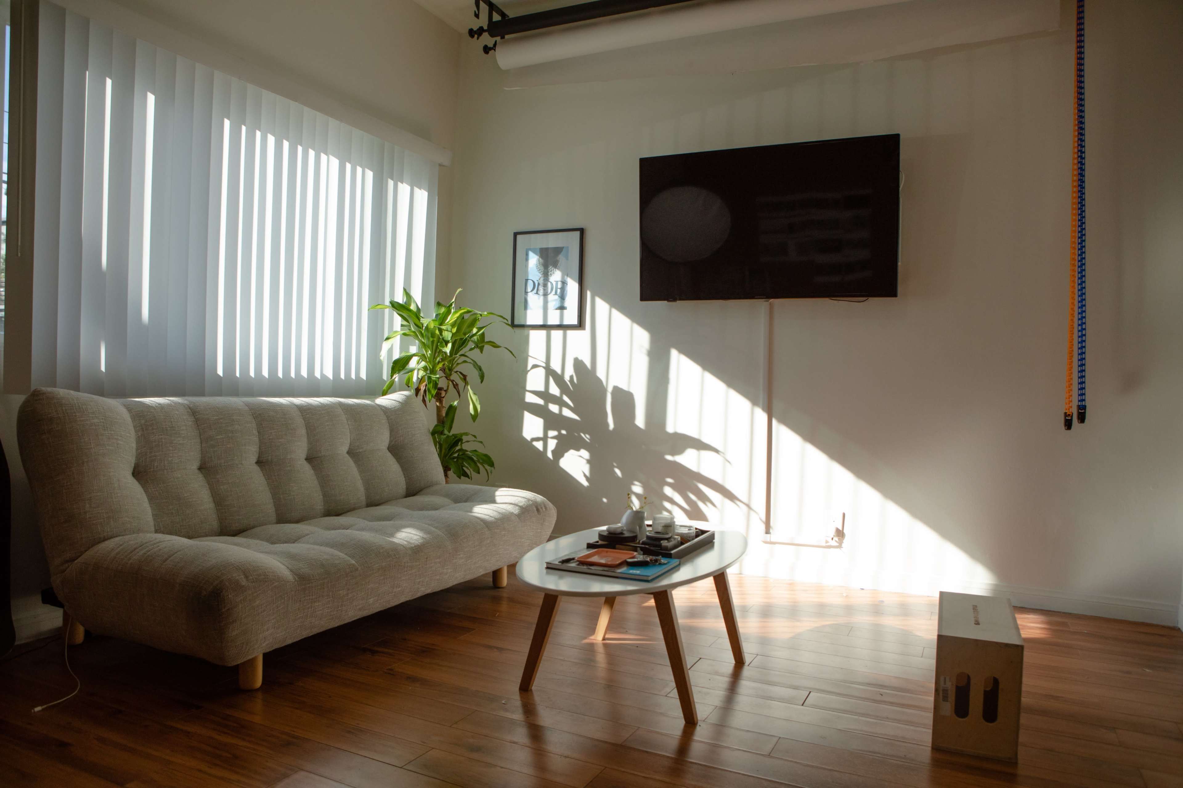 A light-filled living room features a gray sofa, a wooden coffee table with decor, and a television mounted on the wall.