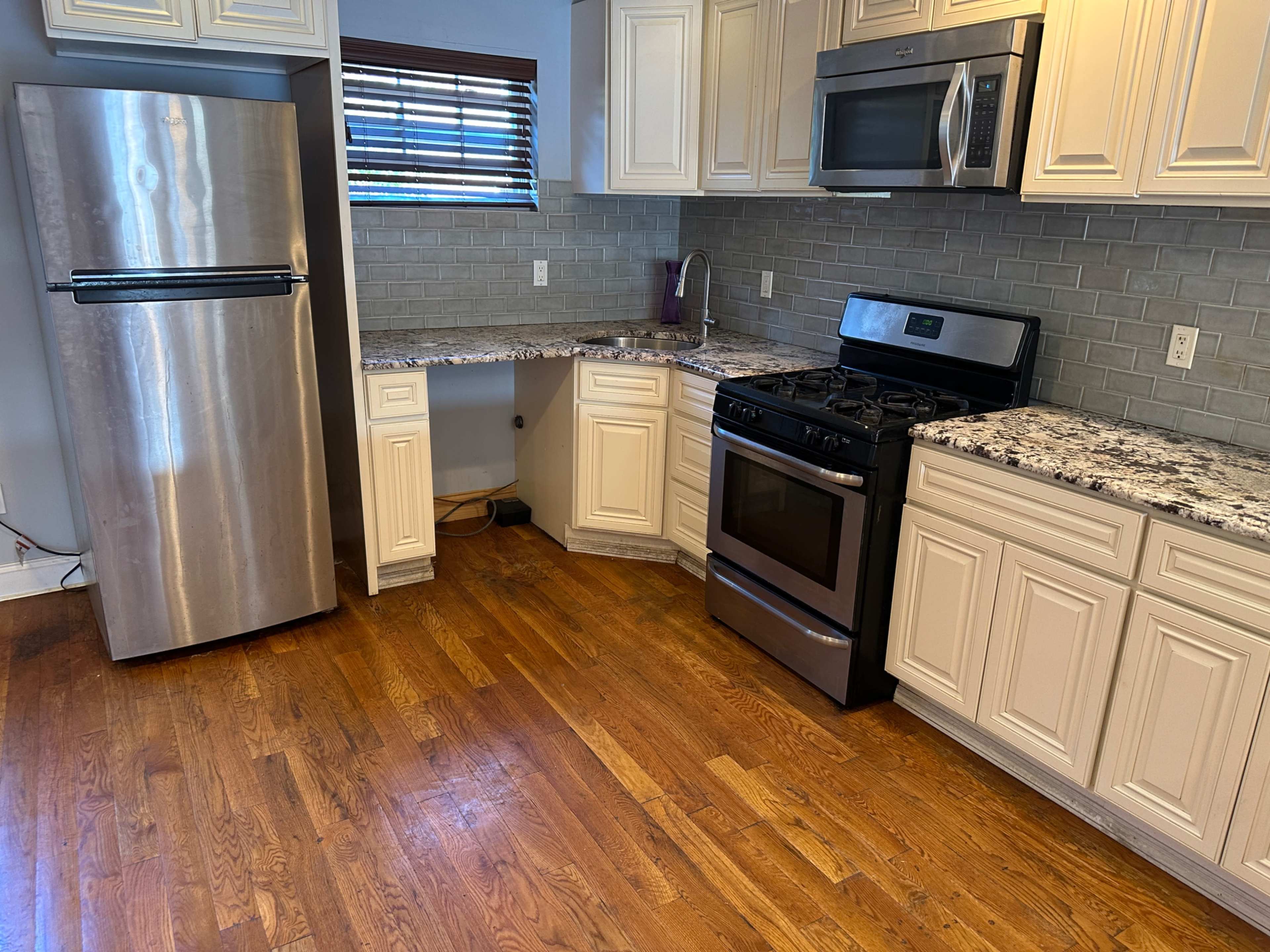 The image shows a kitchen with stainless steel appliances, including a refrigerator and a gas stove, along with white cabinets and a granite countertop.