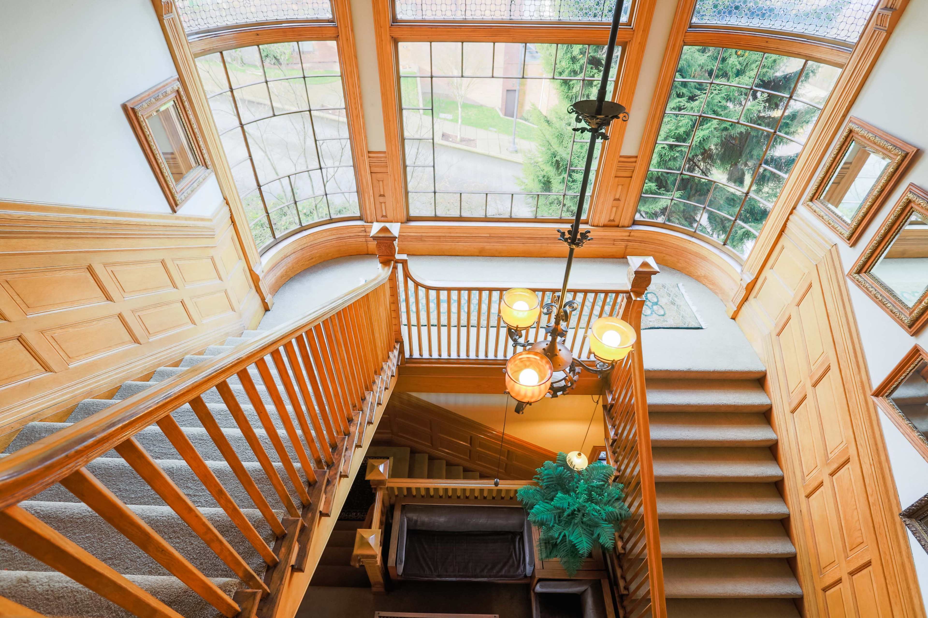 A spacious wooden staircase with a decorative chandelier, leading to a well-lit landing with large windows.
