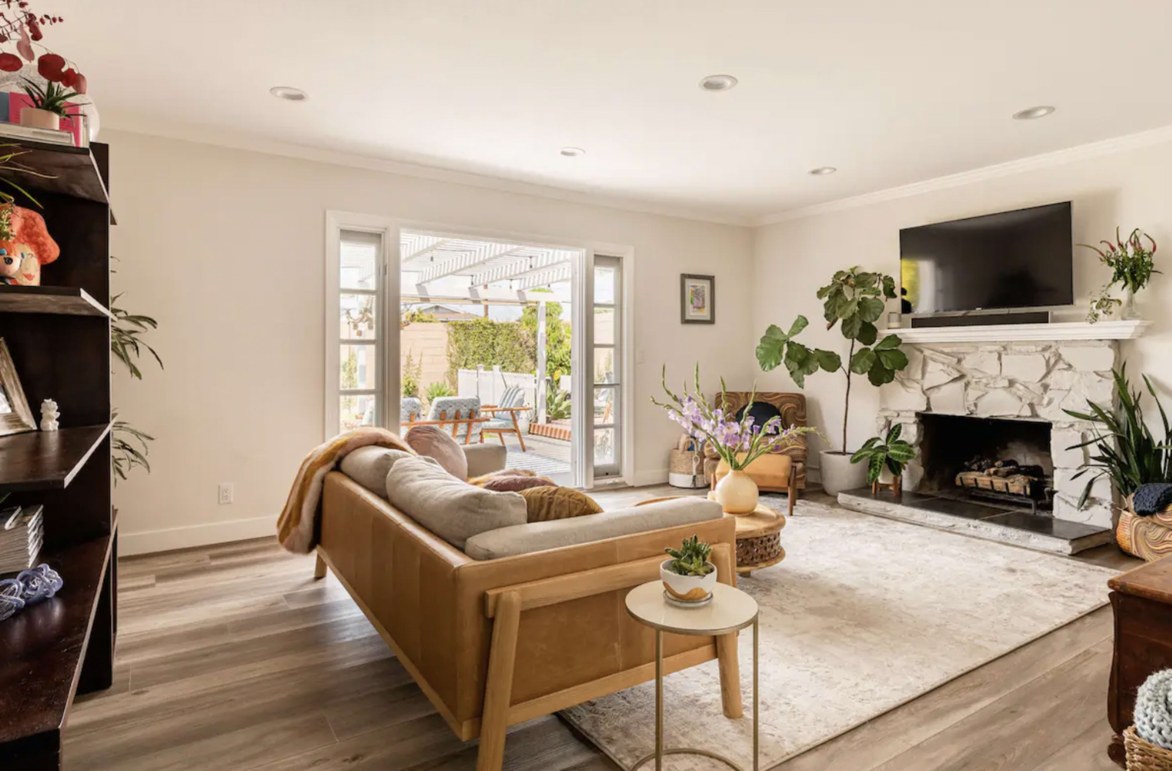 The living room features a beige sectional sofa, a marble fireplace, and large windows overlooking a patio garden.