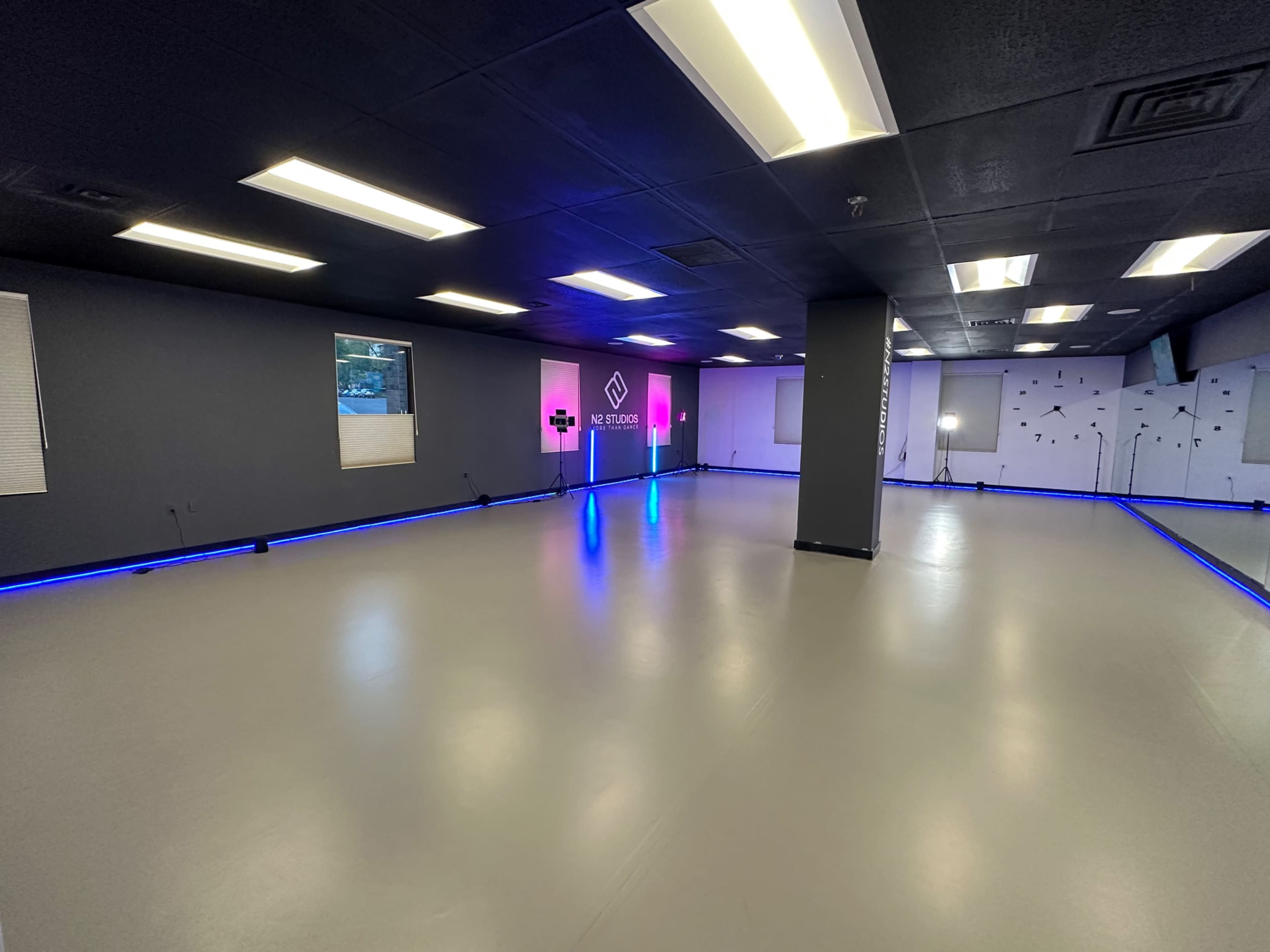 A spacious, empty studio with gray walls, a polished floor, and colorful LED lighting along the edges.