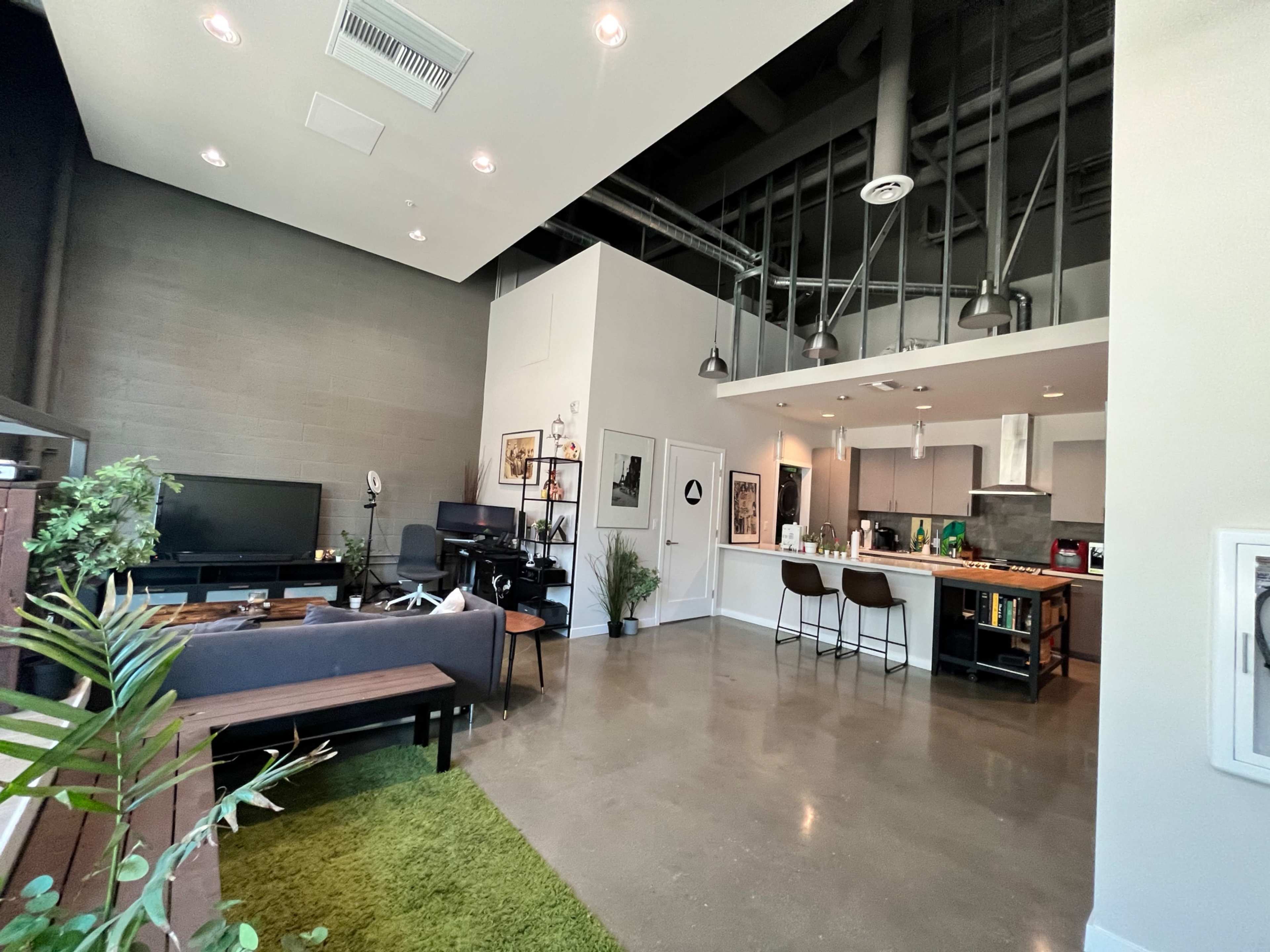 A modern, open-concept living space featuring a living area with a dark sofa, a small dining bar, and a kitchen with sleek appliances.