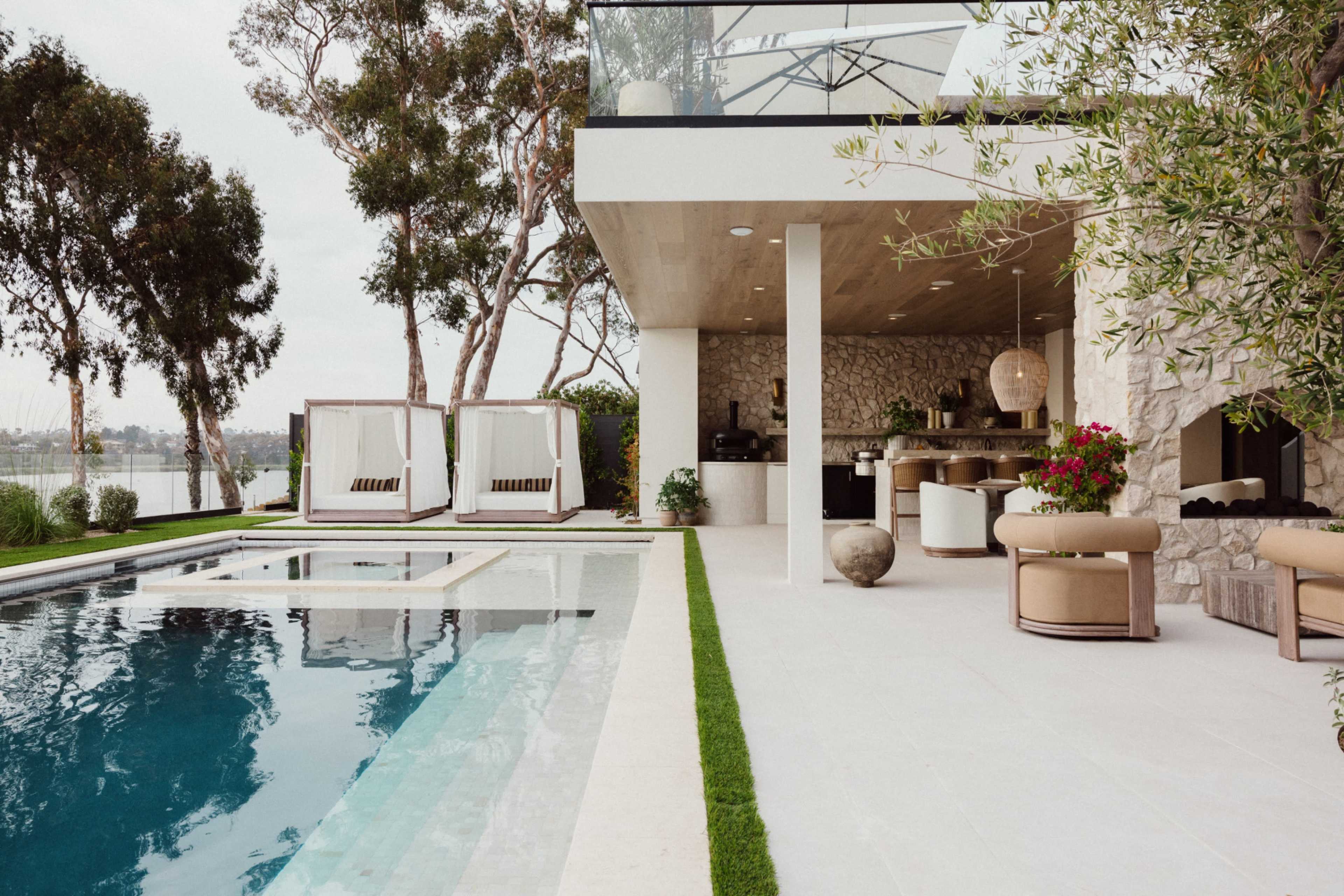 A modern outdoor space features a swimming pool, loungers, and cabanas, adjacent to a stylish indoor area with stone accents and a large glass wall.