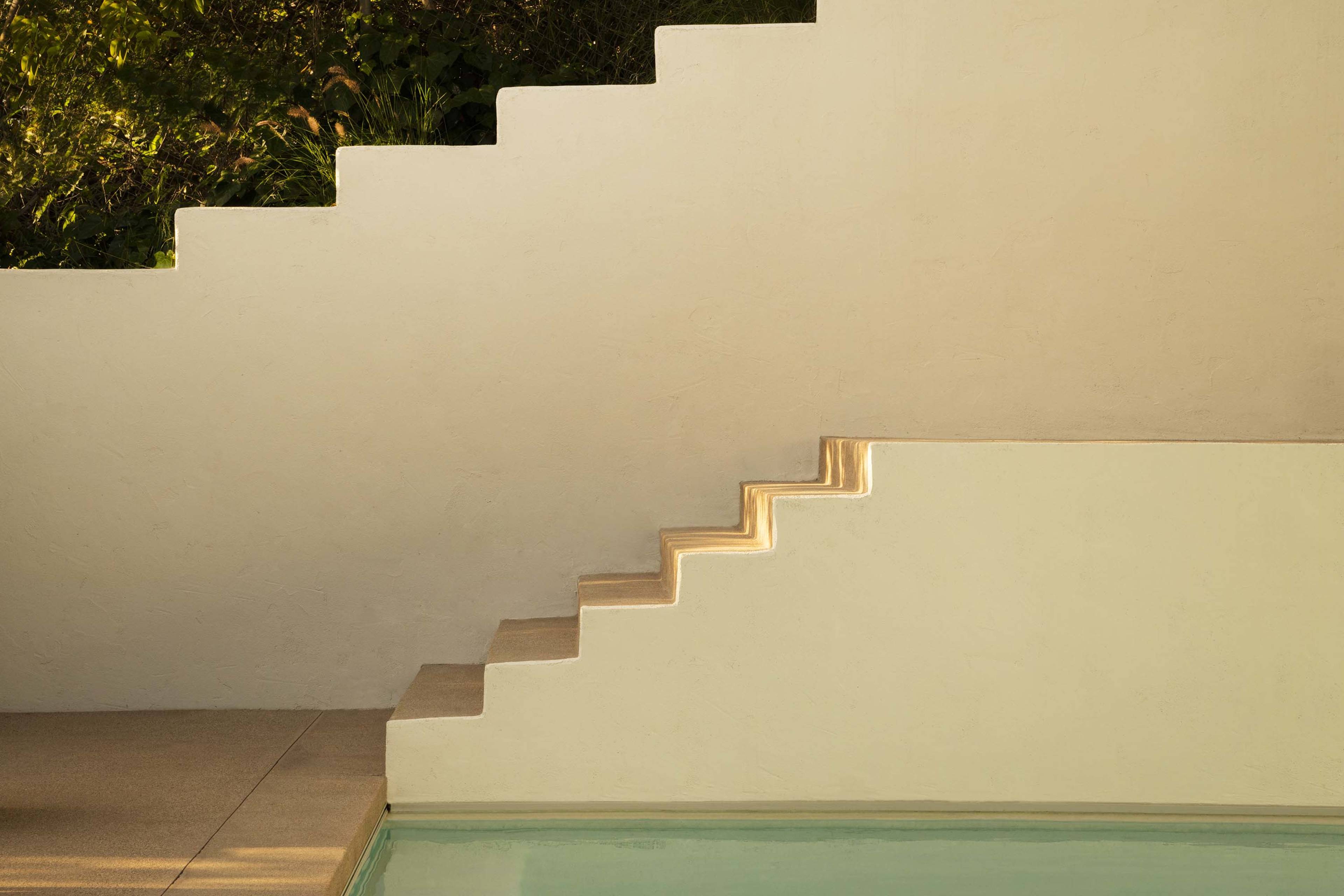 A minimalist architectural feature of steps leading up to a textured wall beside a pool.