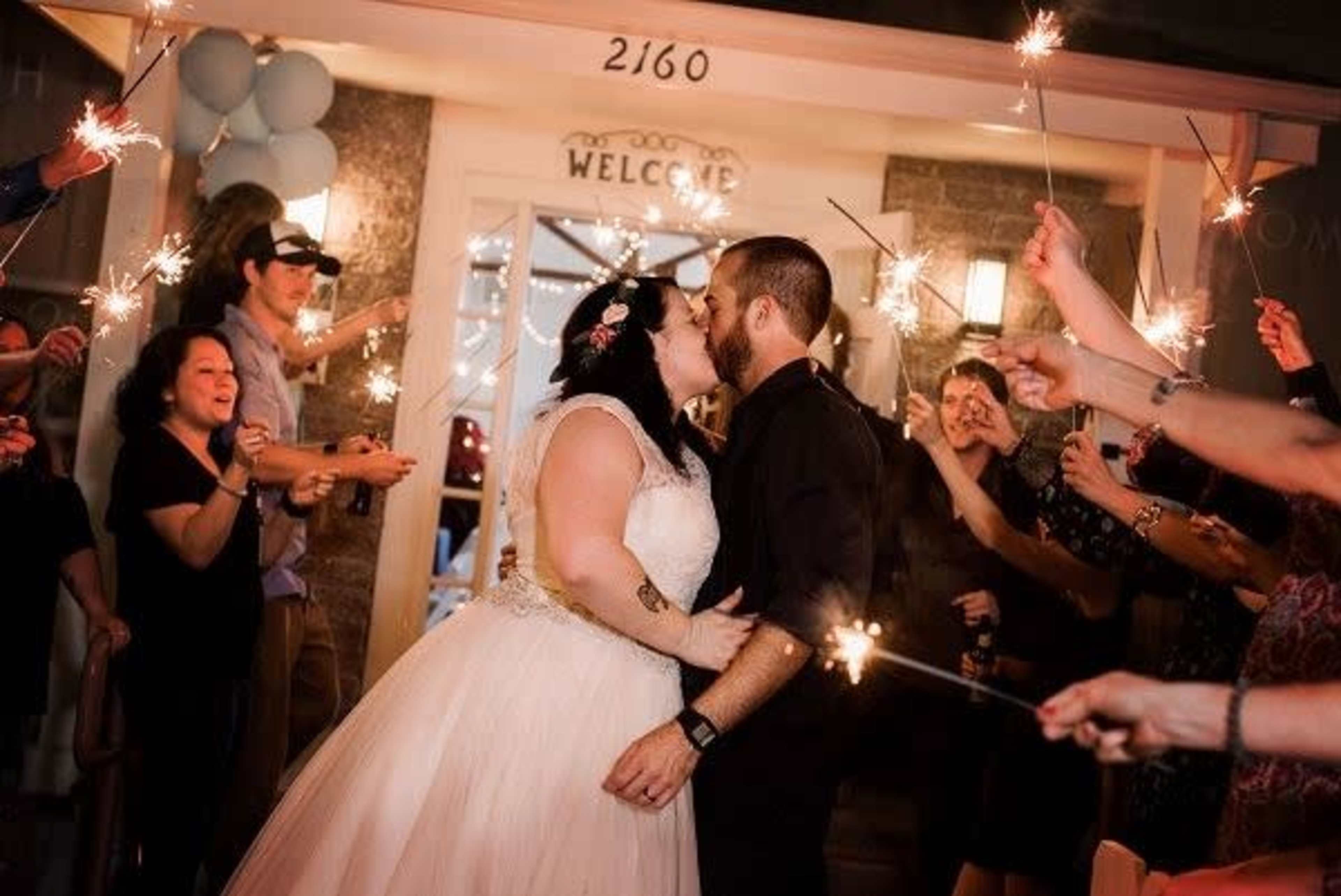 A bride and groom kiss while surrounded by guests holding sparklers in celebration.