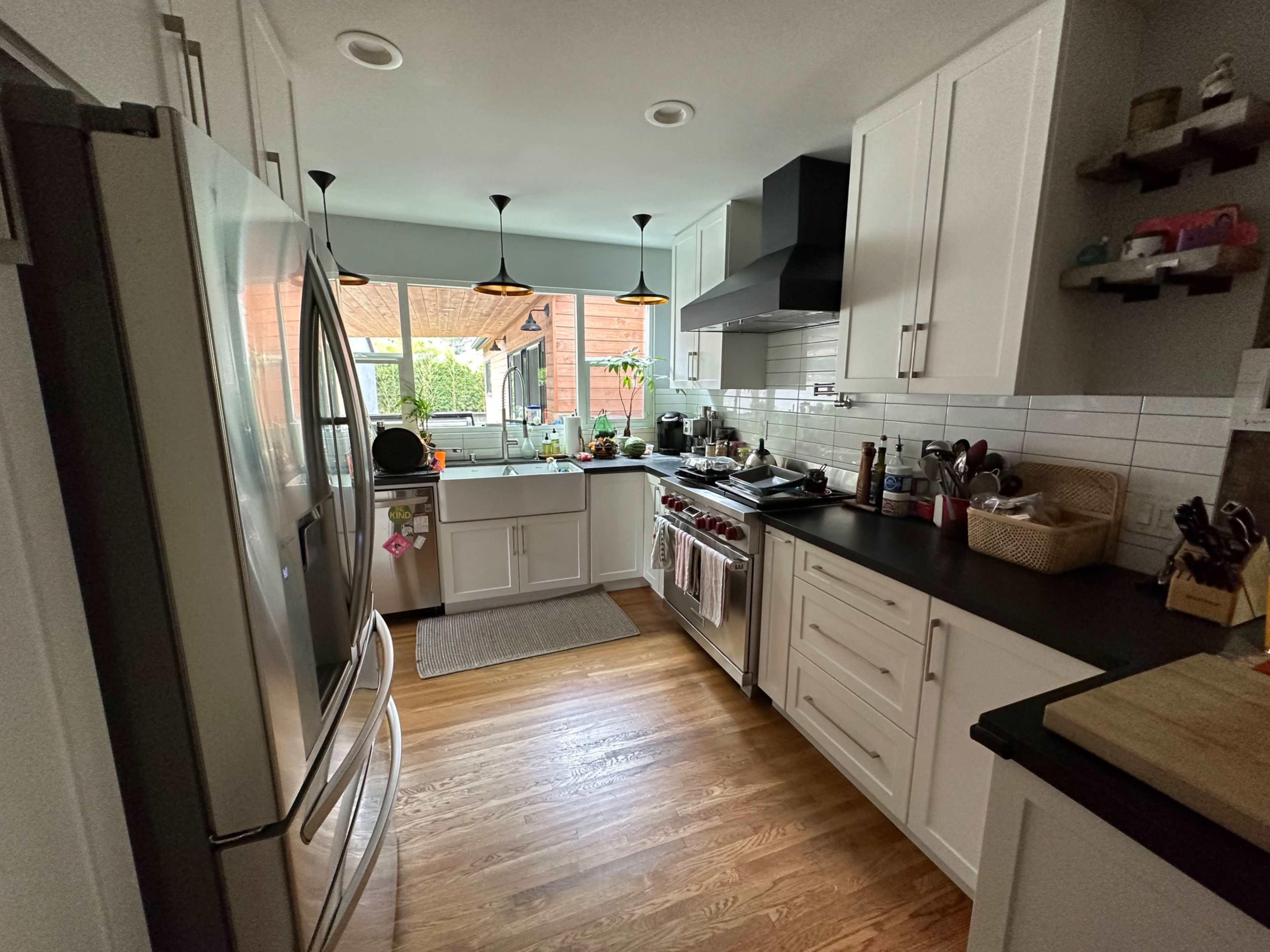 A modern kitchen with stainless steel appliances, white cabinetry, and a wooden floor, featuring a mix of cooking utensils and ingredients on the countertops.