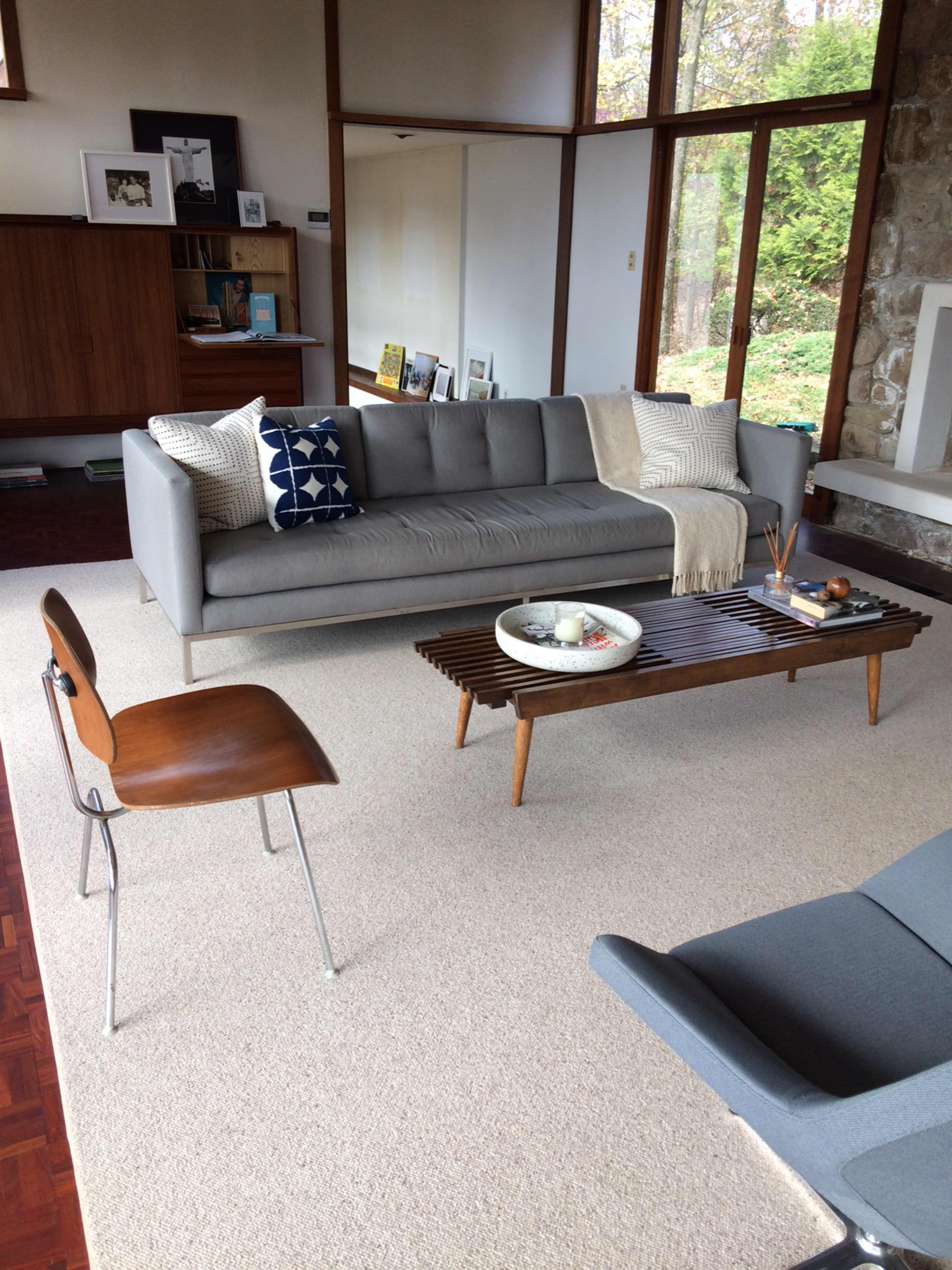 A modern living room features a gray sofa with decorative pillows, a wooden coffee table with an arrangement of items, and large windows that allow natural light to fill the space.