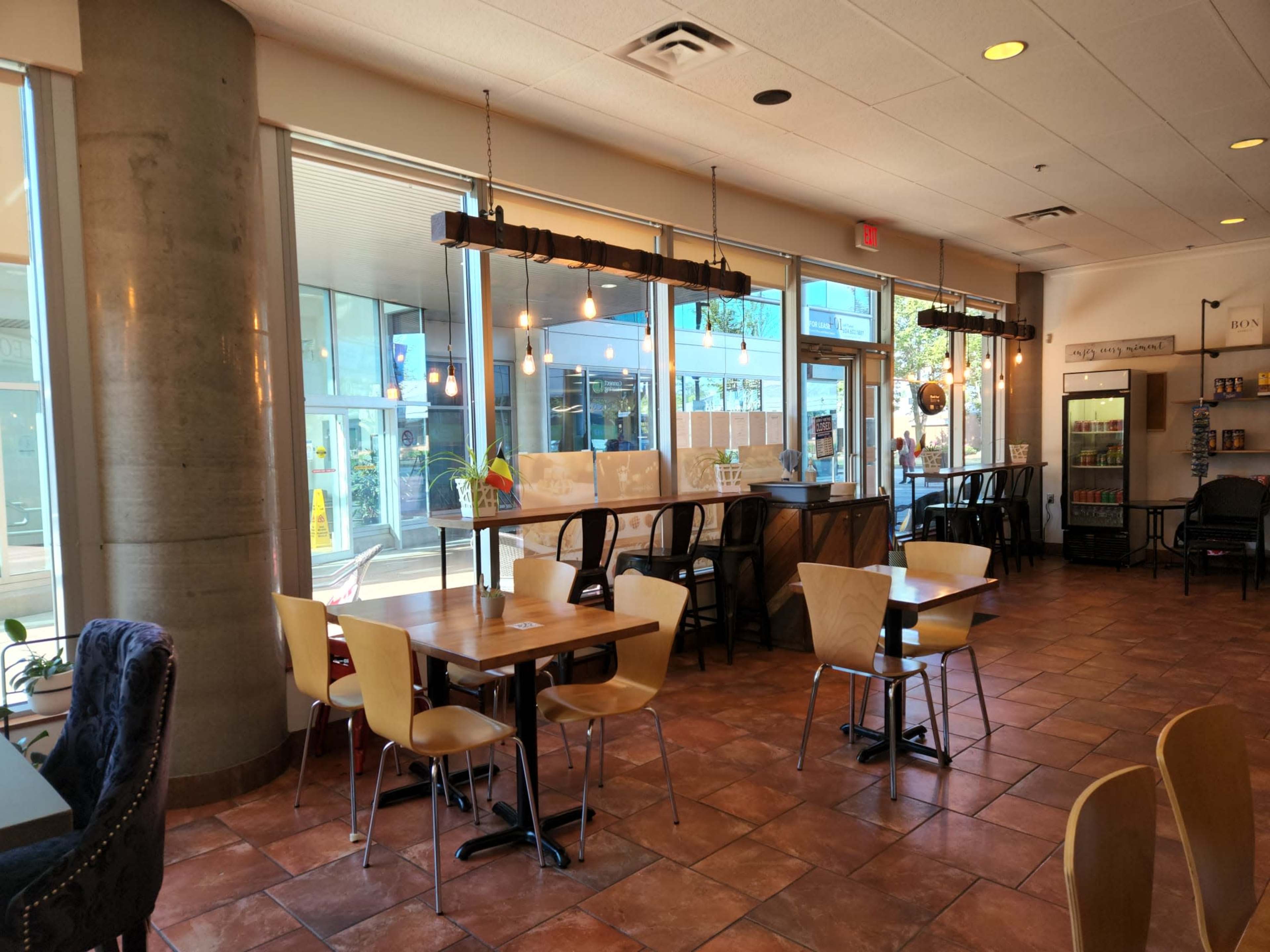 A café interior with tables and chairs, large windows letting in natural light, and a bar counter with hanging lights.