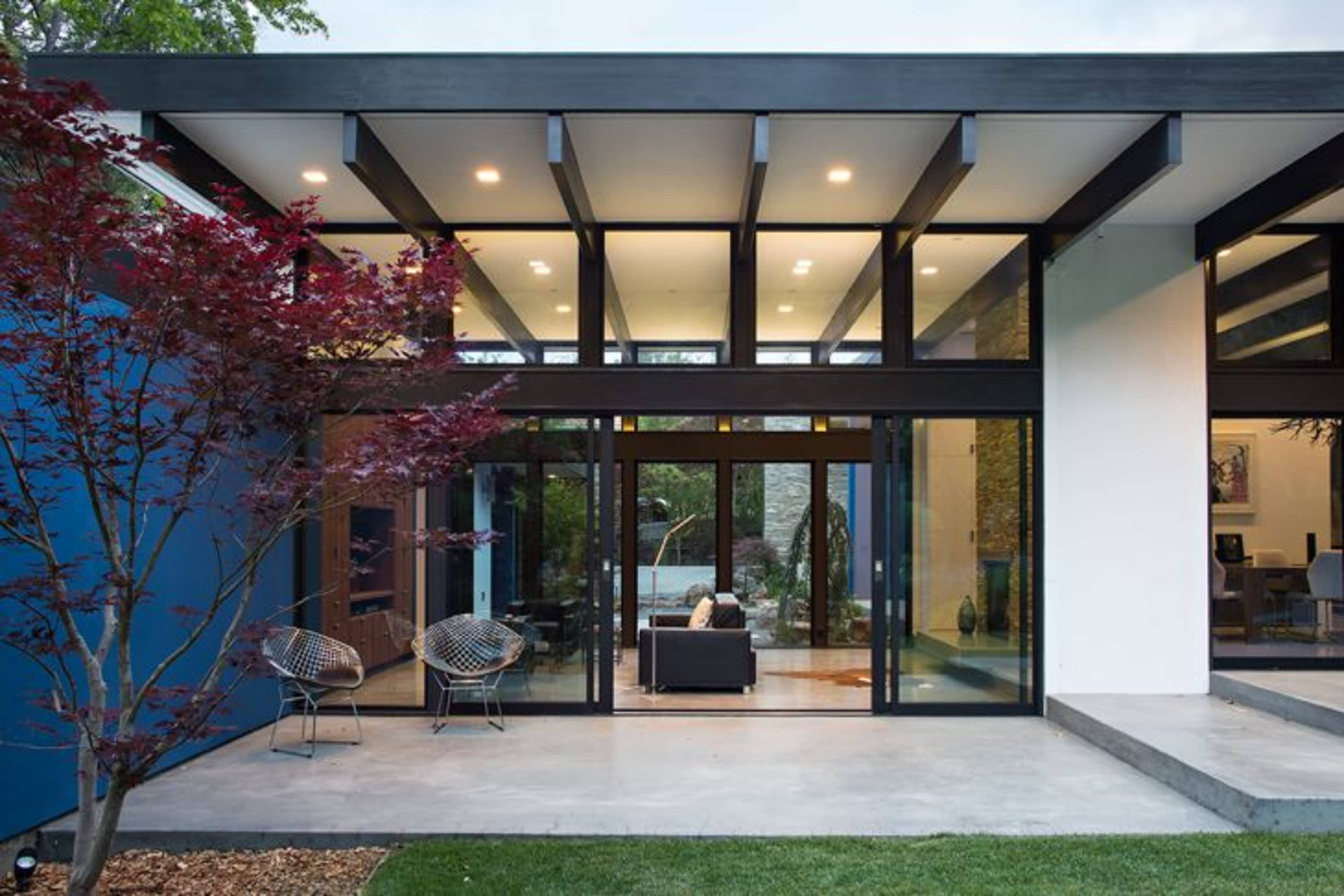 A modern house features large glass doors that open to a landscaped garden, with a sleek interior visible through the transparent walls.