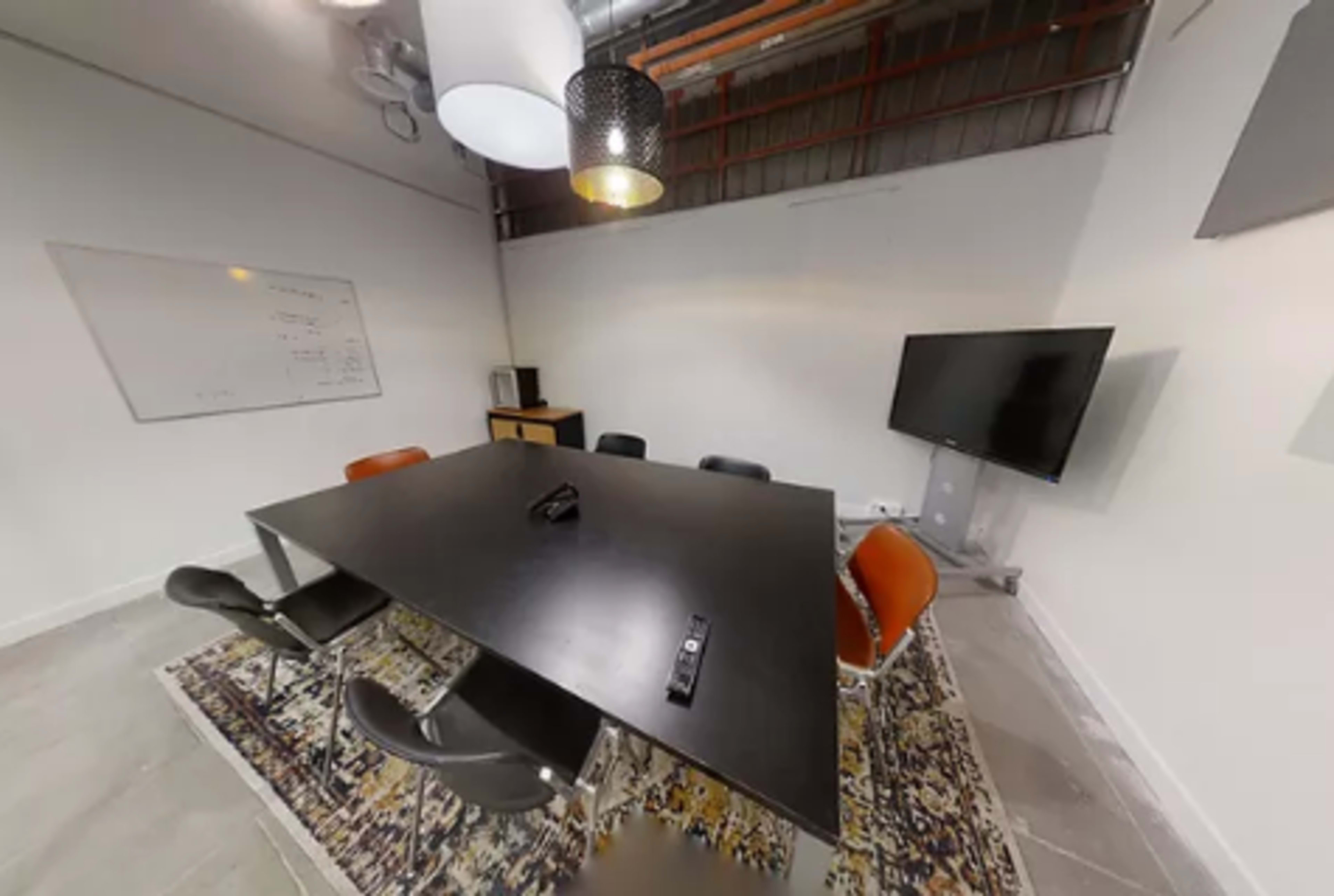 A modern conference room features a large black table surrounded by chairs, a television, and a whiteboard.
