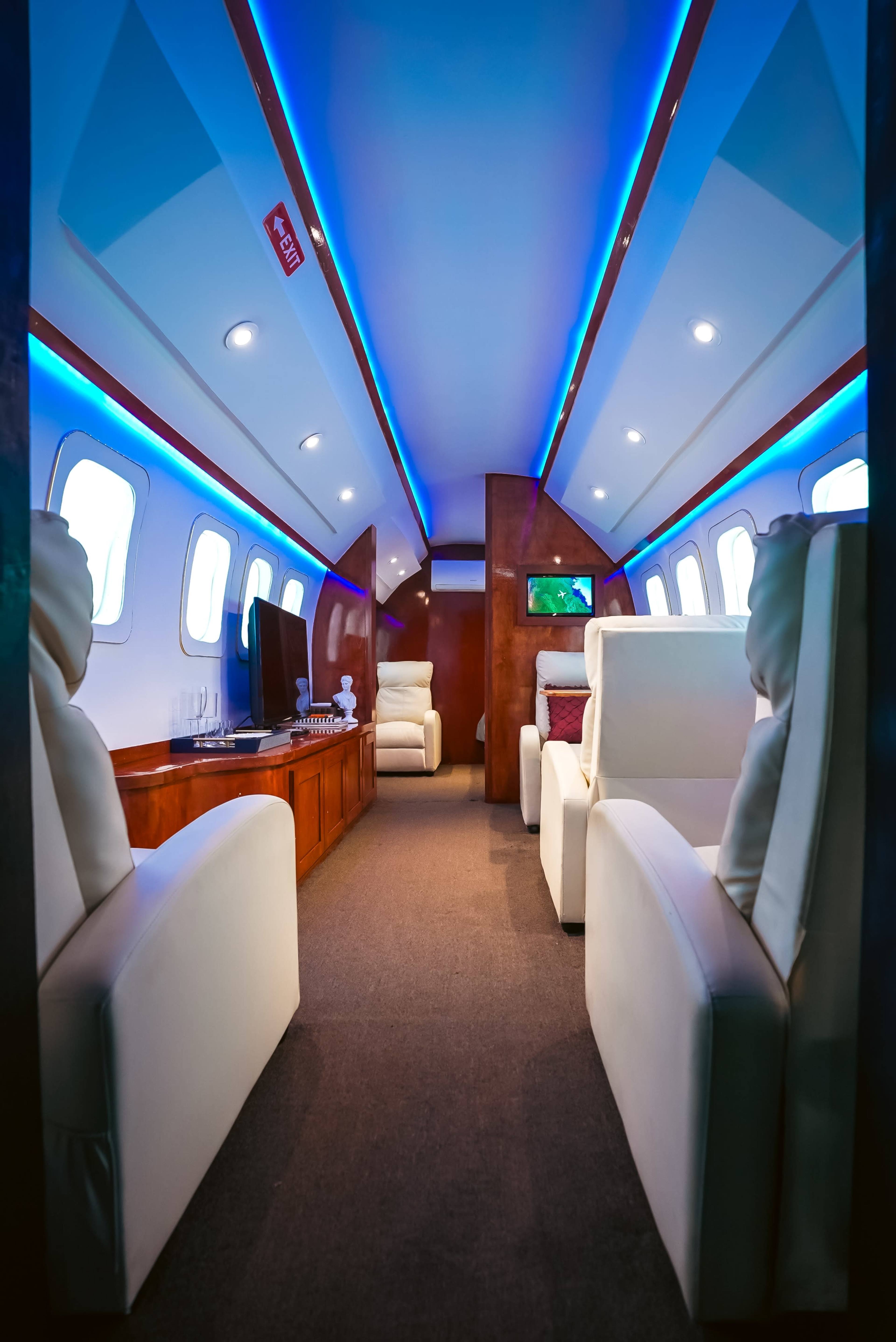 The image shows the interior of a private jet featuring white seating, wooden accents, and blue LED lighting along the ceiling.