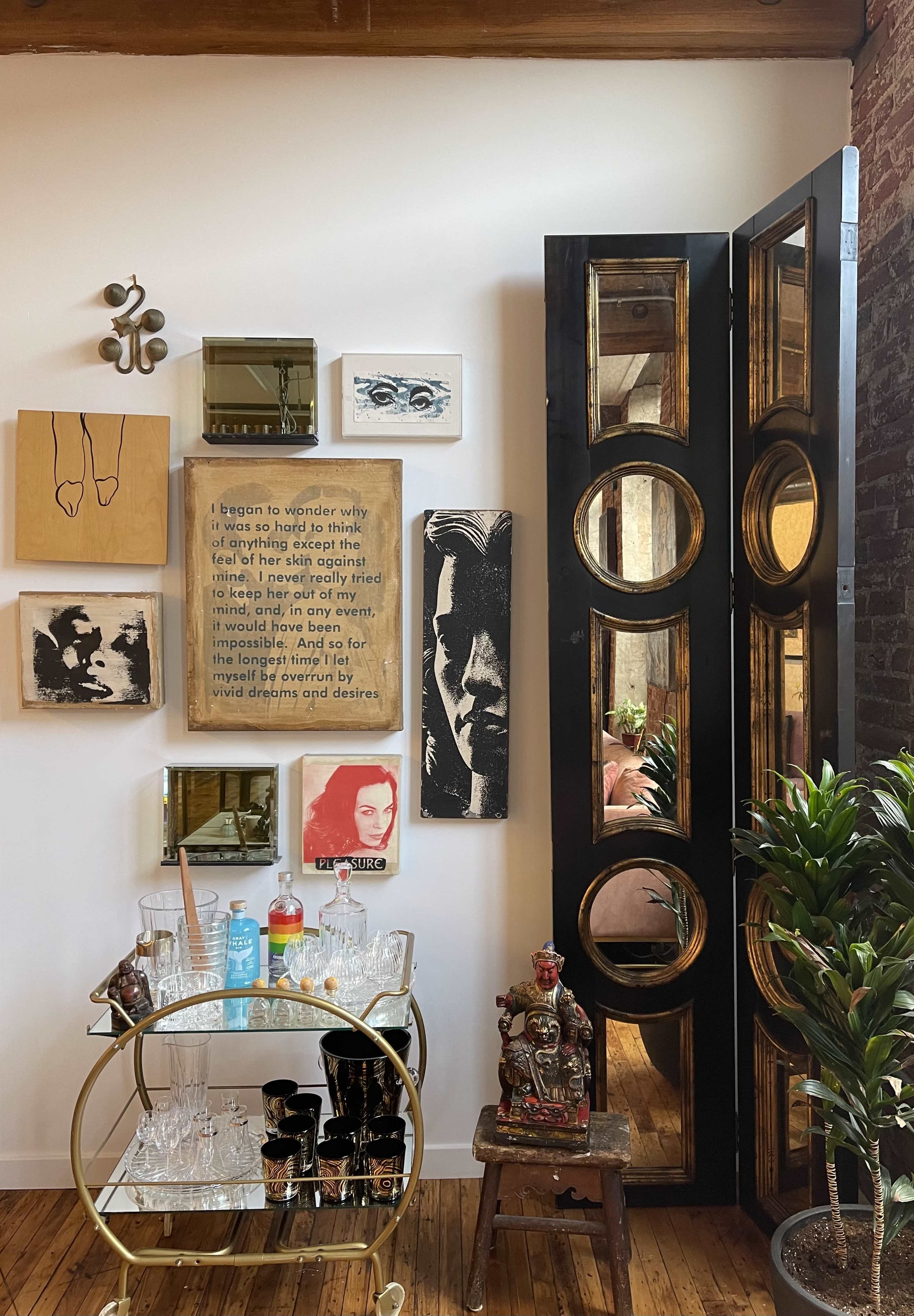 The image shows a corner of a room with a bar cart displaying glassware, framed artwork on the wall, and a decorative folding screen with circular cutouts.