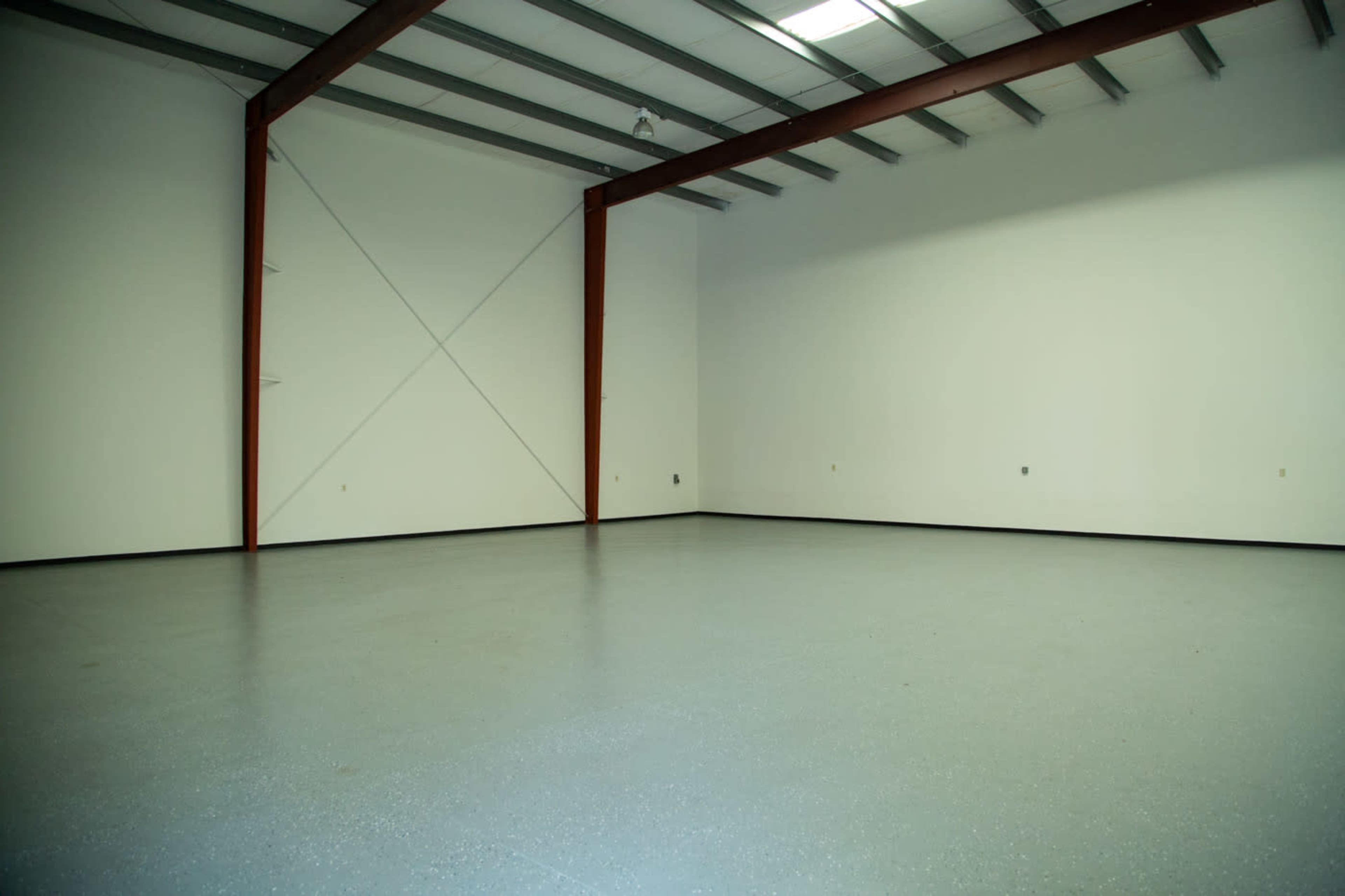 A large, empty industrial space with concrete flooring and metal beam structures supporting the ceiling.