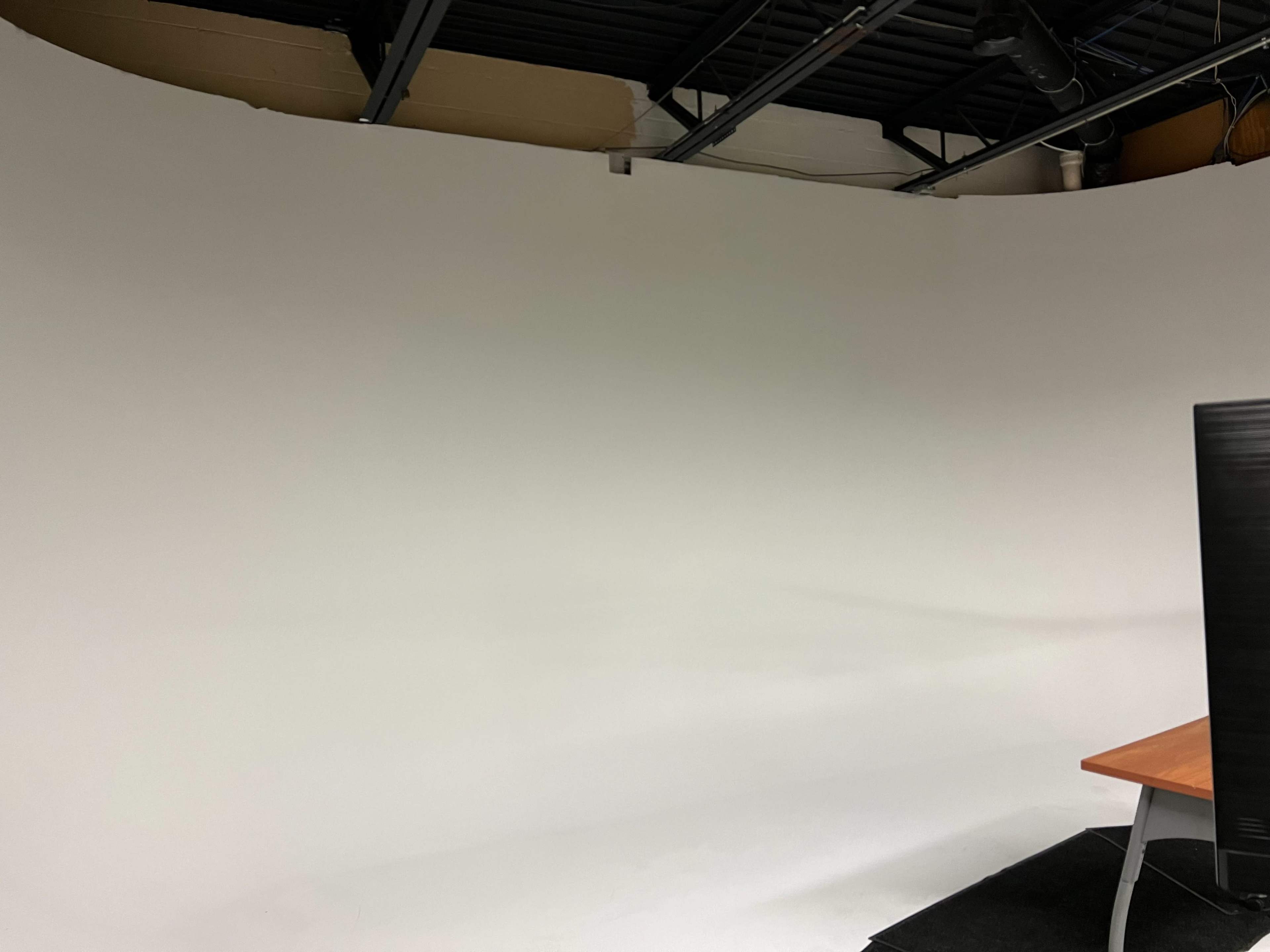 A blank, white backdrop in a studio setting with a wooden desk and a black computer monitor in the foreground.