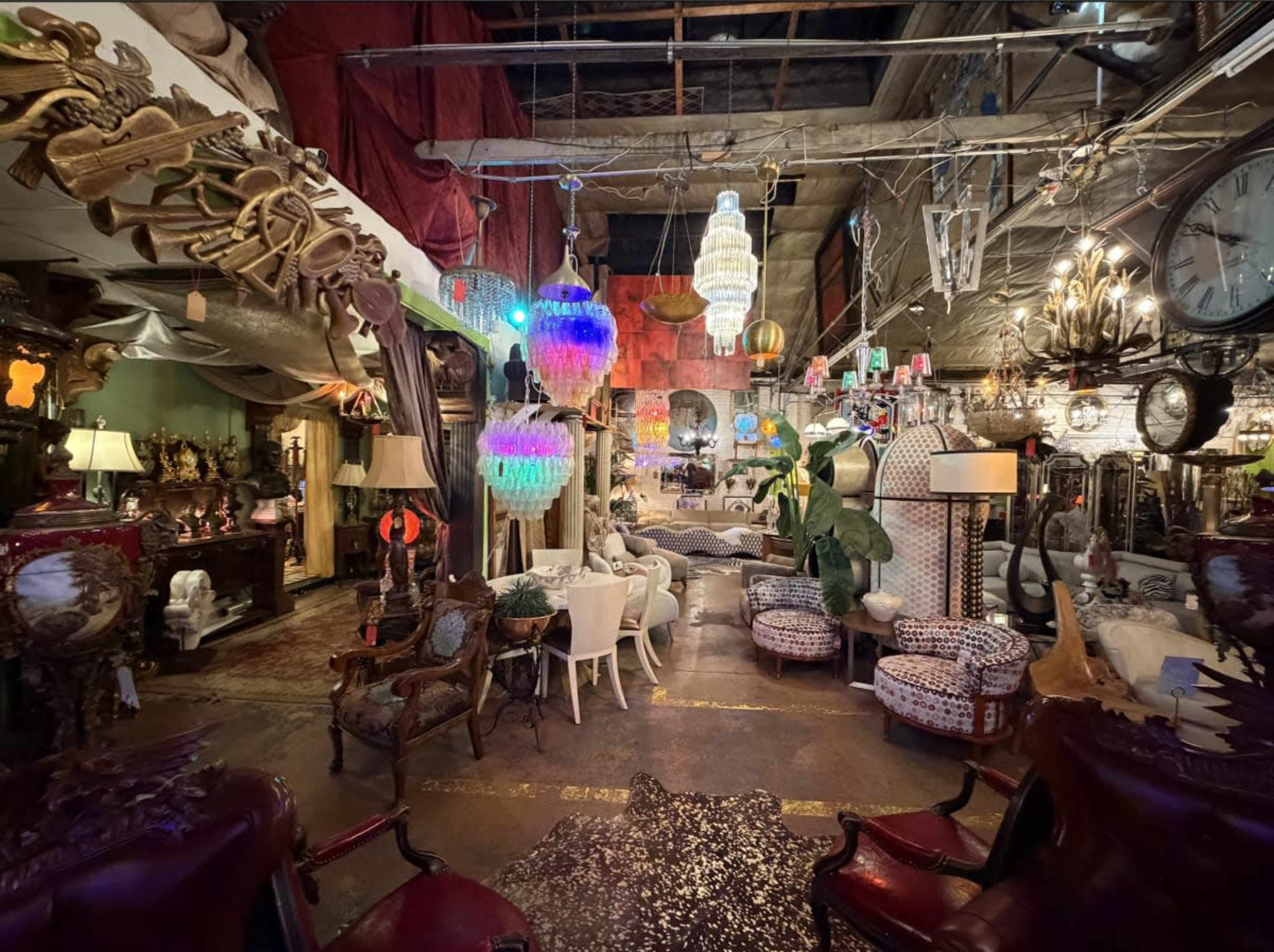 The image shows a vintage-themed store filled with various pieces of furniture and decor, including lamps, chairs, and chandeliers, arranged in a spacious layout.
