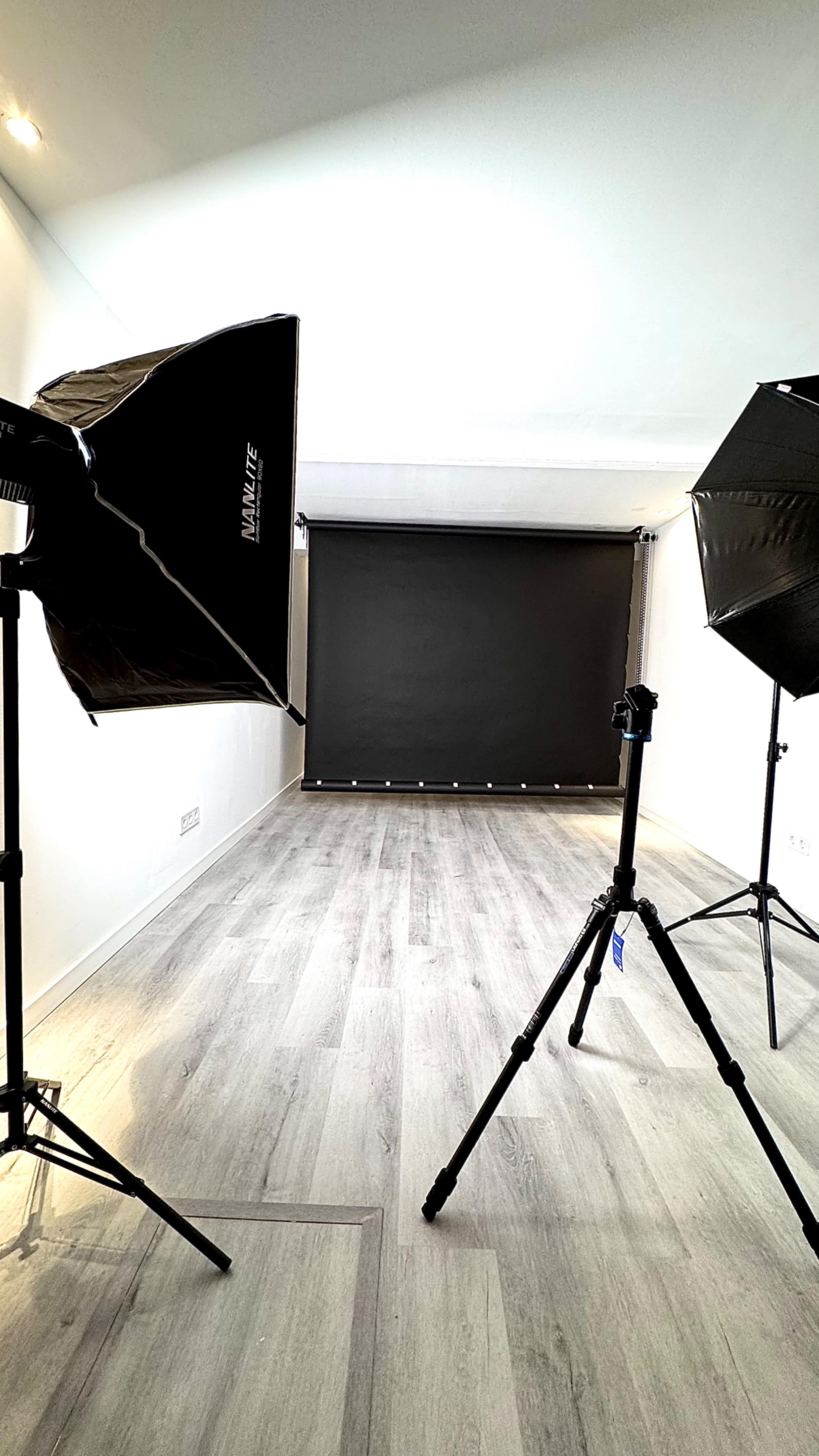 The image shows a well-lit photography studio with two large softbox lights directed towards a black backdrop.