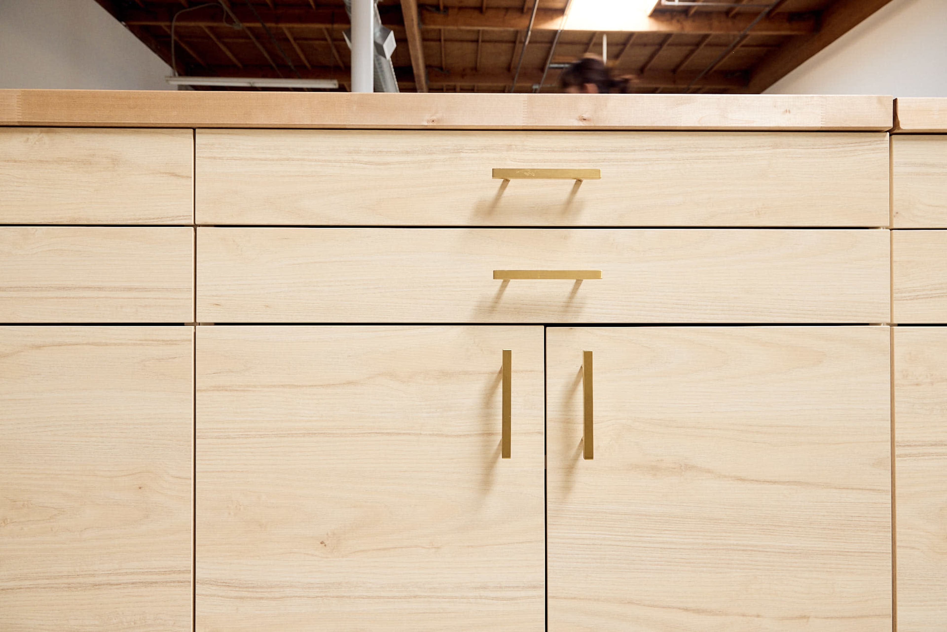 A close-up view of a wooden cabinet with light-colored wood and minimalist brass handles.