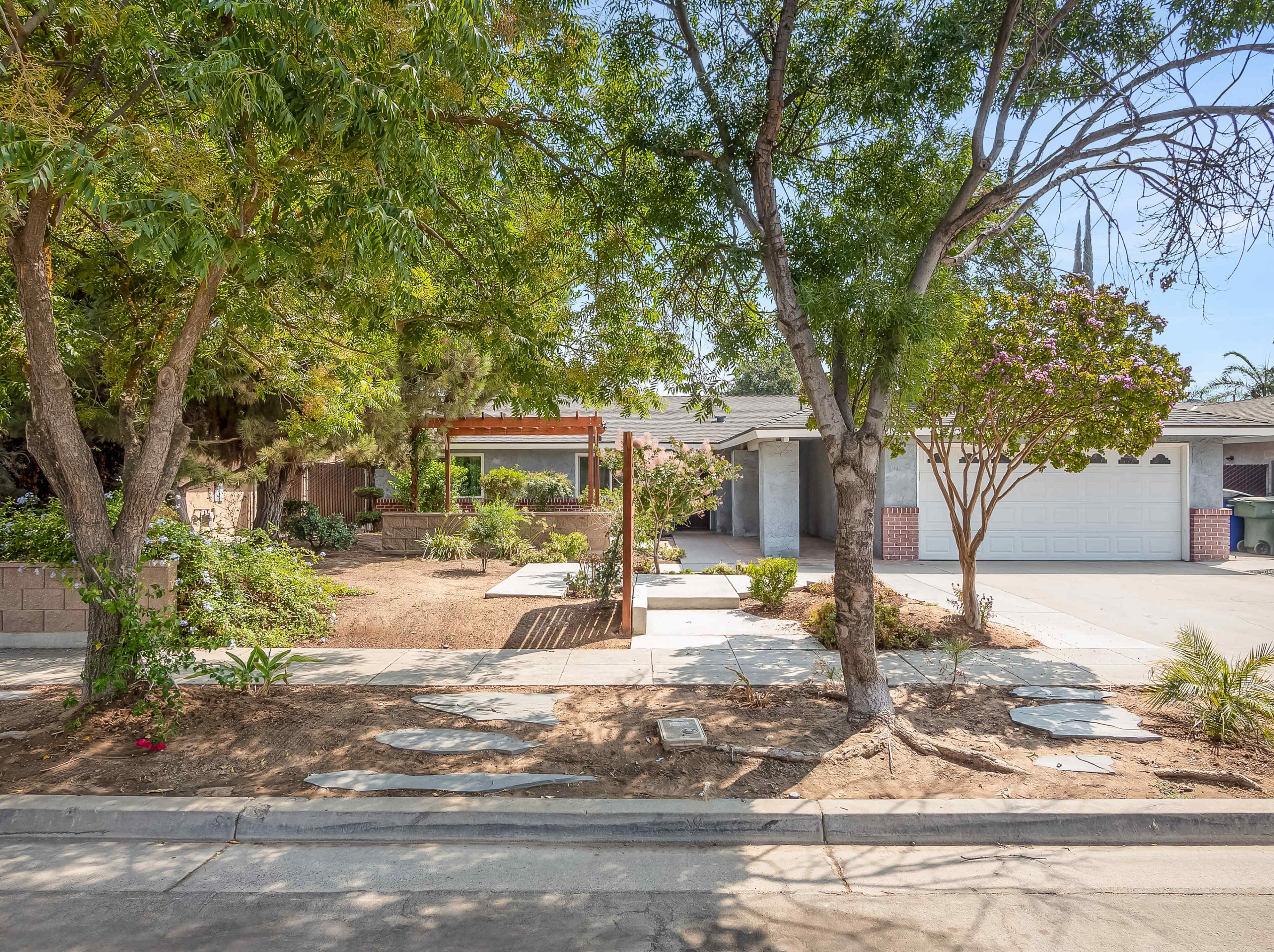 A residential yard with a landscaped area featuring shrubs and trees, alongside a concrete driveway and garage.