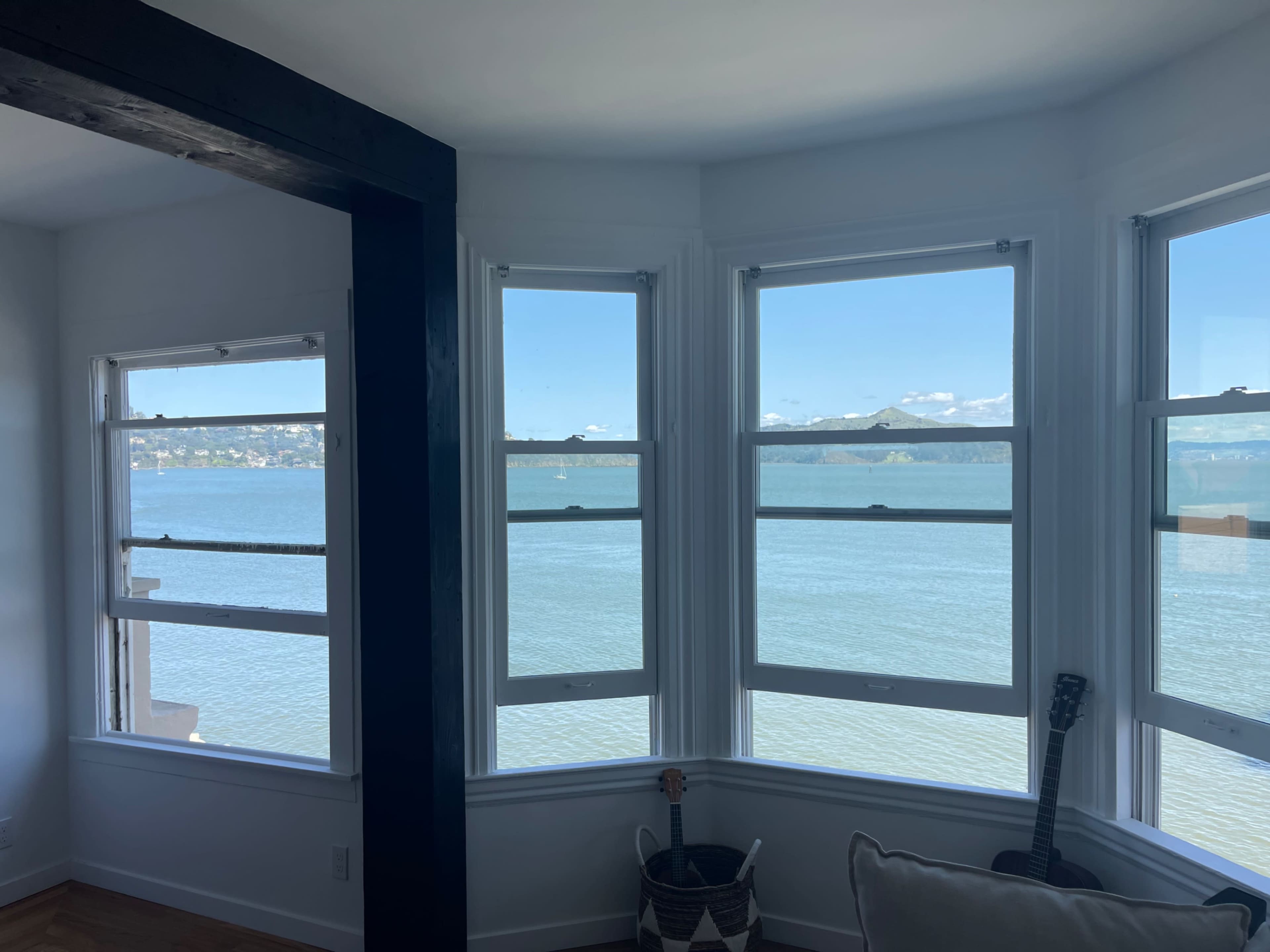 A corner room with three large windows facing a body of water and distant mountains.