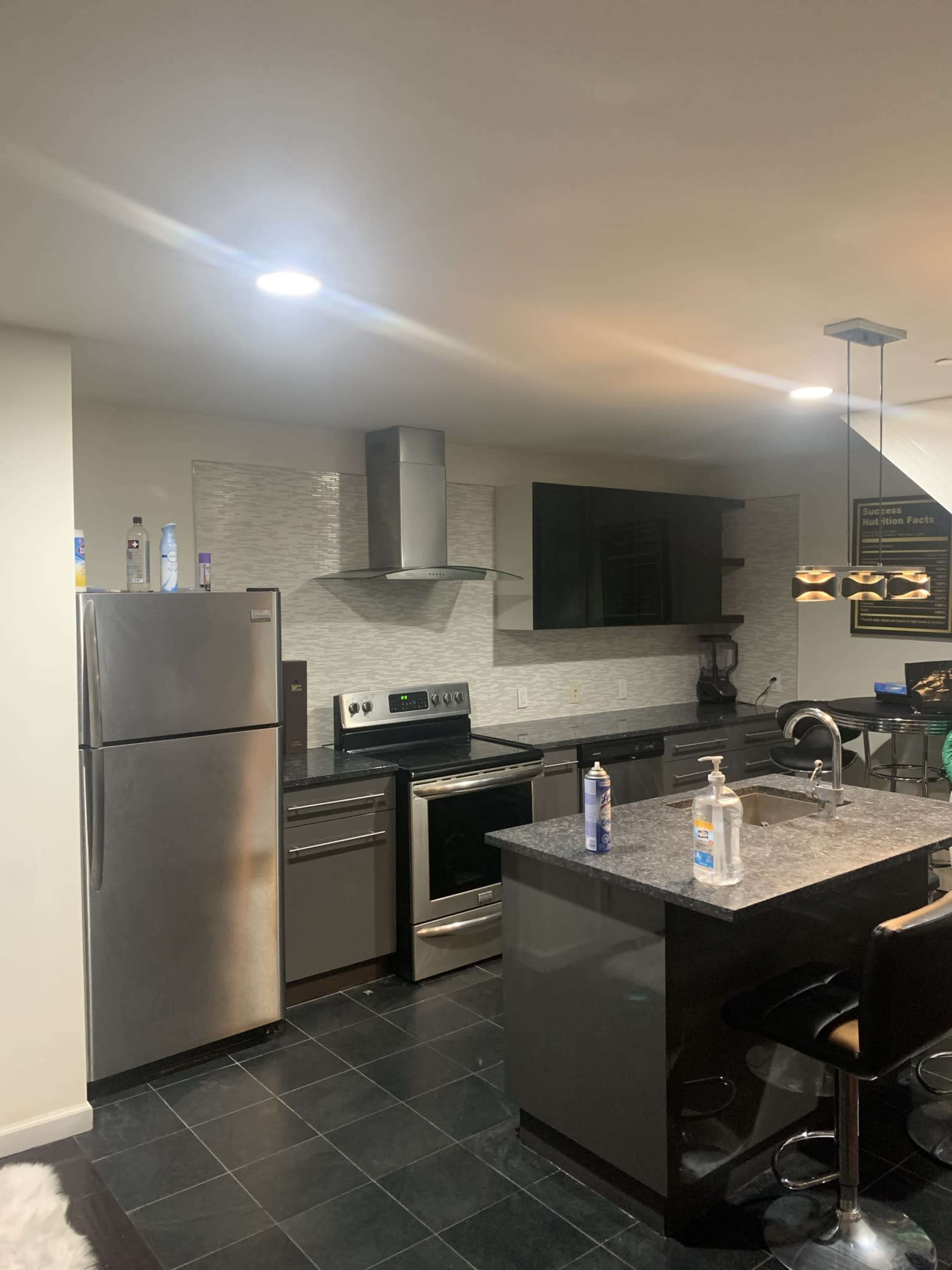 A modern kitchen with stainless steel appliances, including a refrigerator and oven, along with dark cabinetry and a granite countertop.