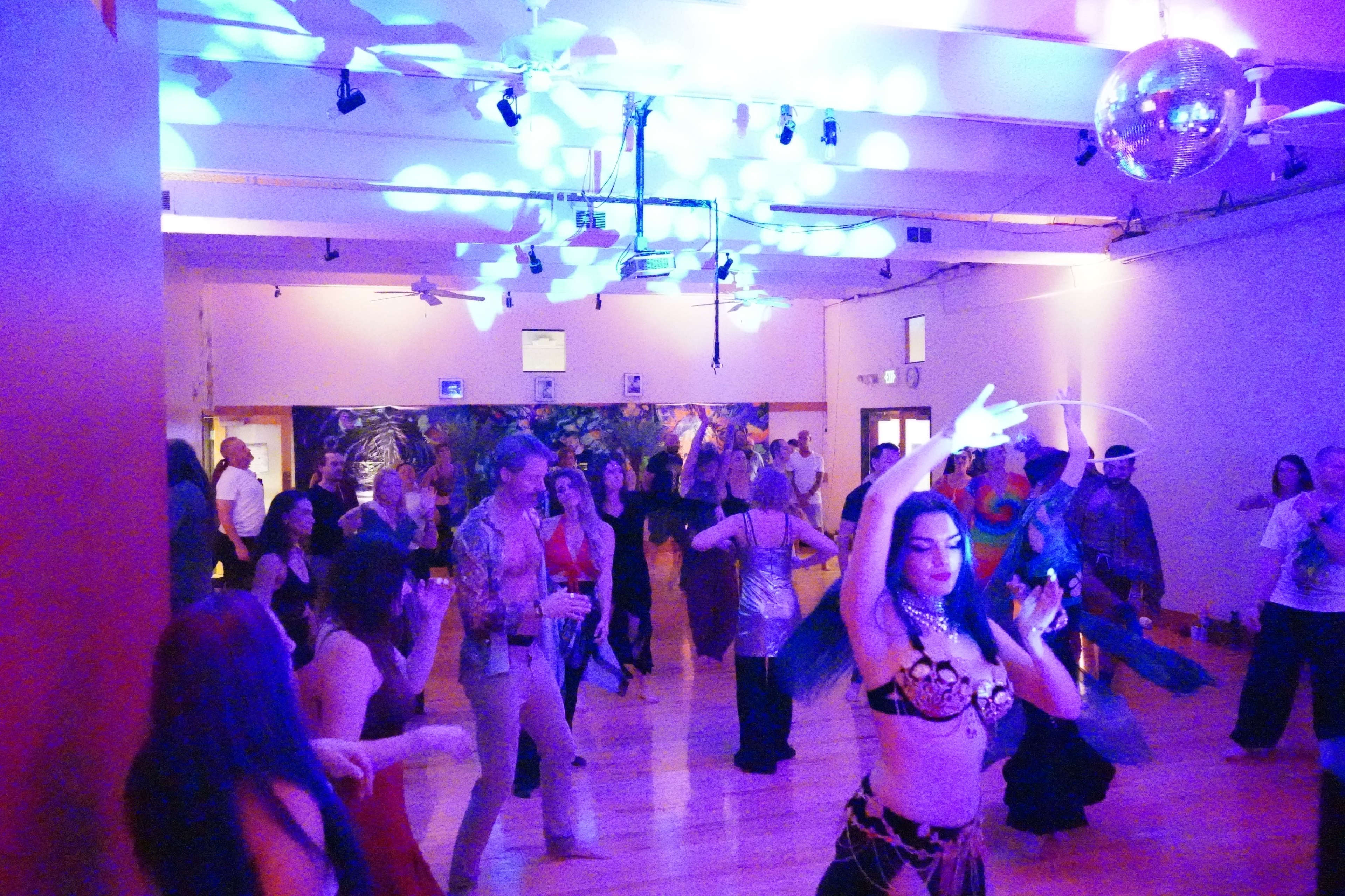 A vibrant dance party scene features a group of people dancing in a well-lit space adorned with a disco ball and colorful lights.