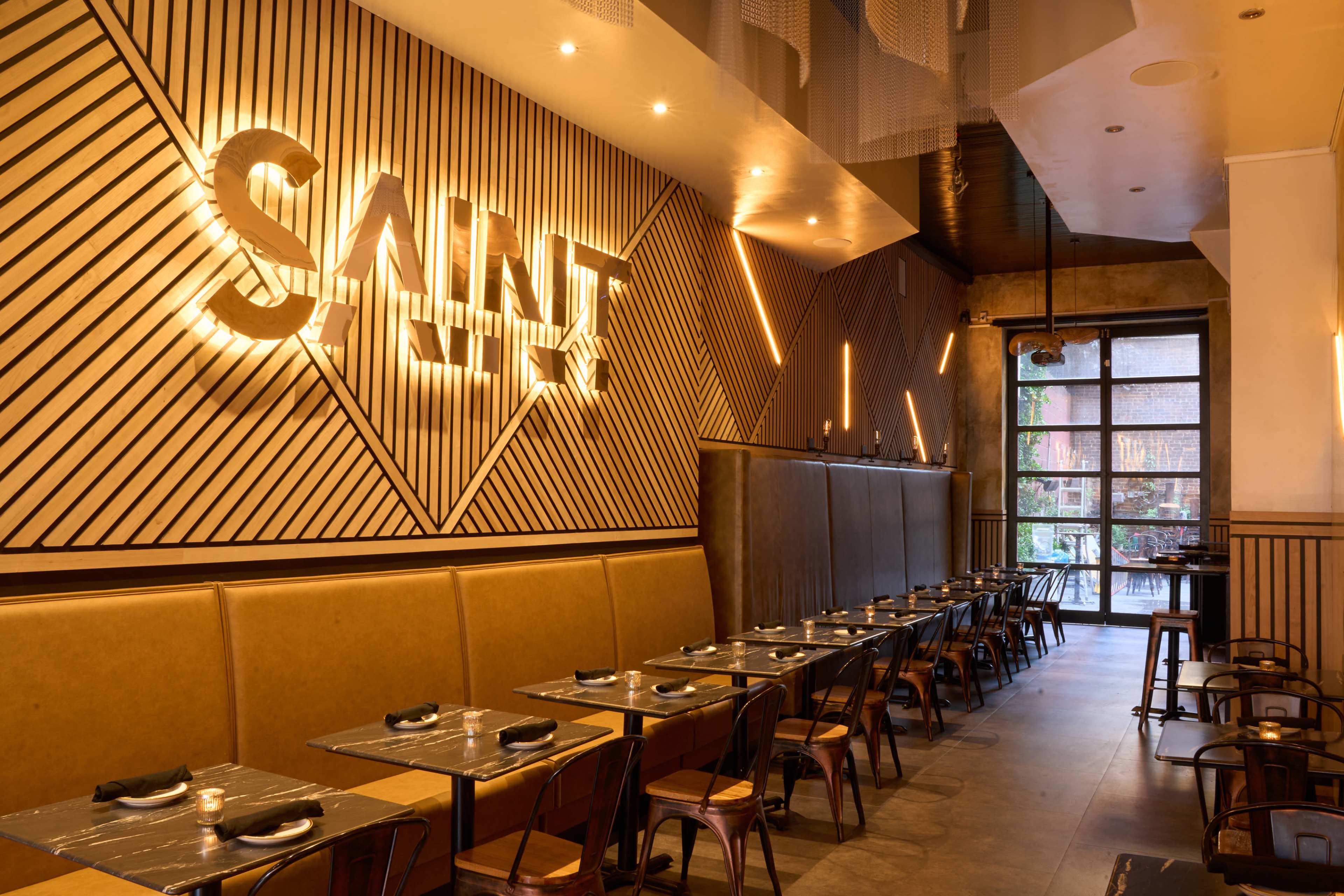 The image shows a modern restaurant interior featuring a linear wood panel design, ambient lighting, and a row of tables with chairs arranged along one side.