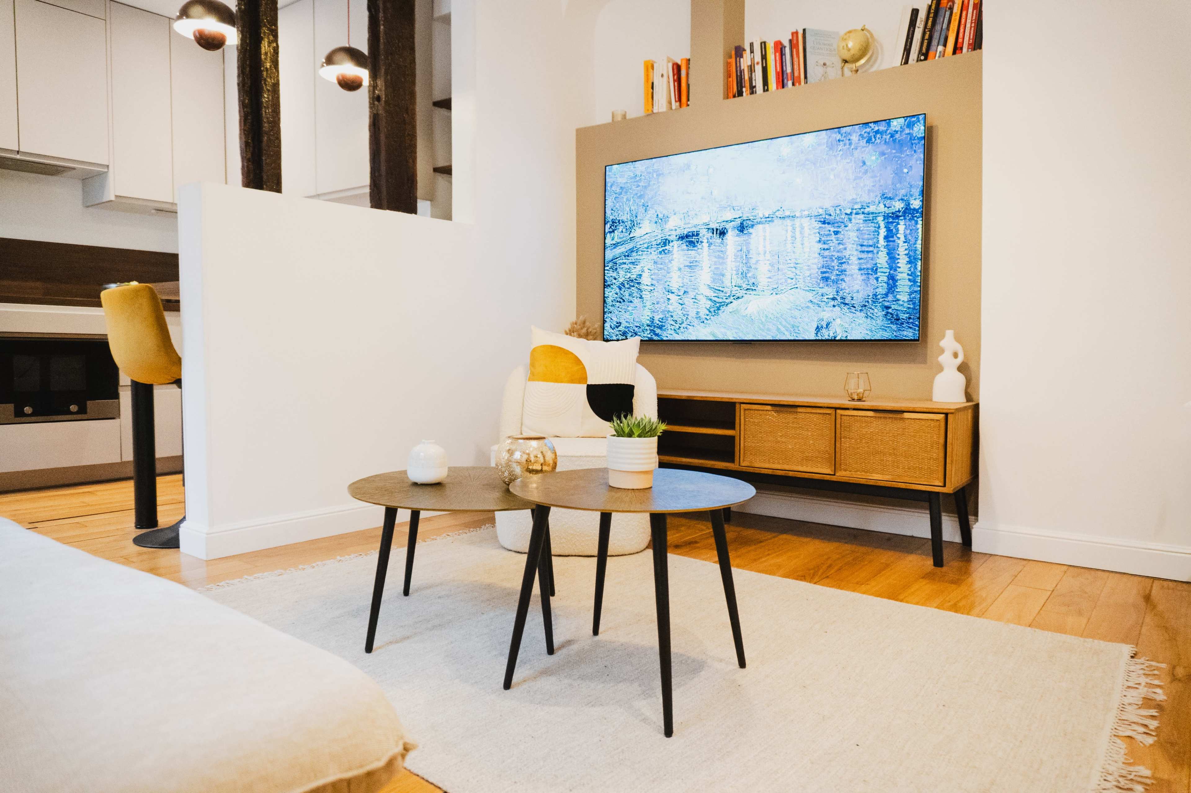 A modern living room features a large television mounted on the wall above a wooden media console, with a coffee table in front and a rug on the floor.