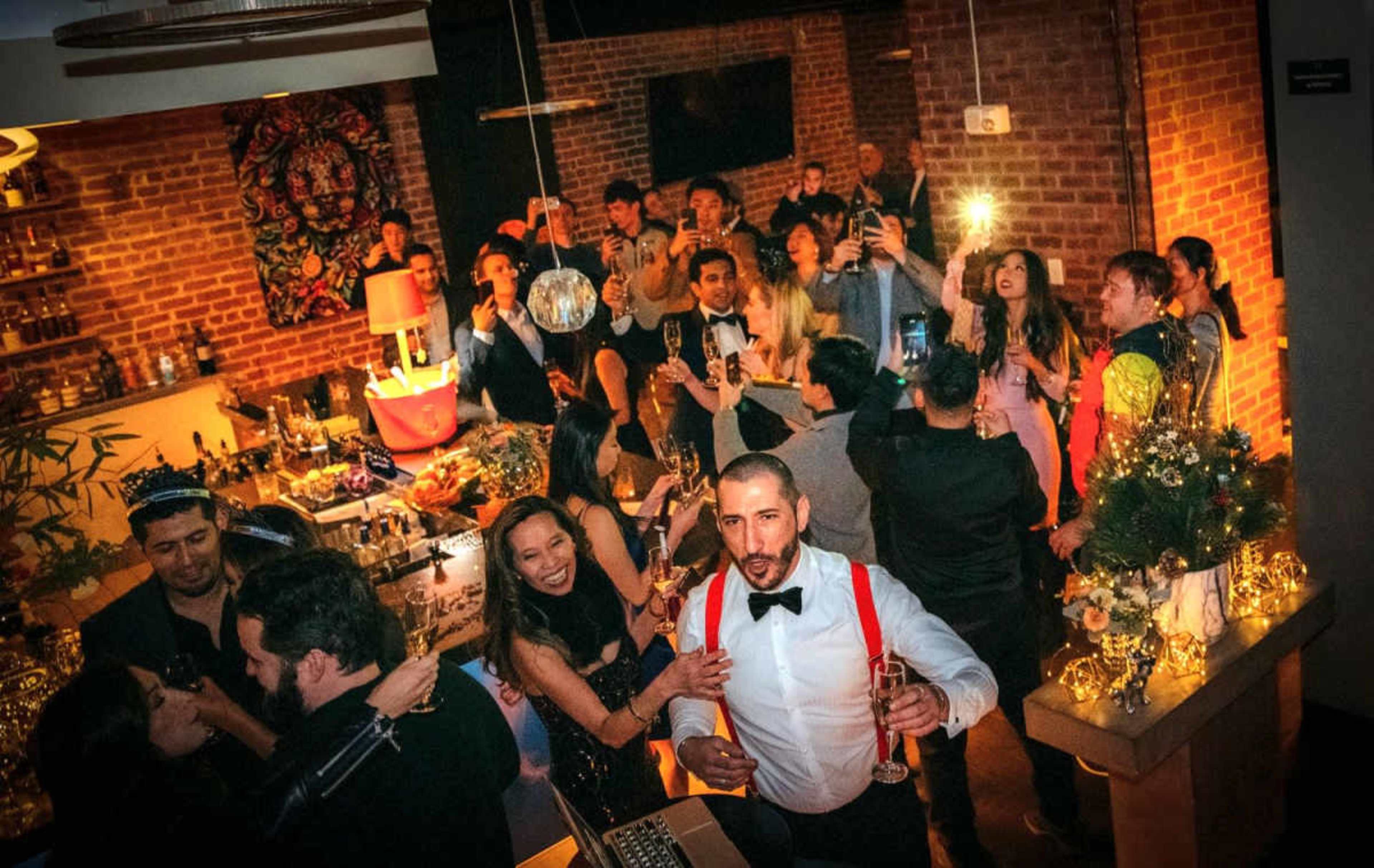 A lively gathering takes place in a well-decorated bar, with groups of people celebrating and raising glasses amidst a festive atmosphere.