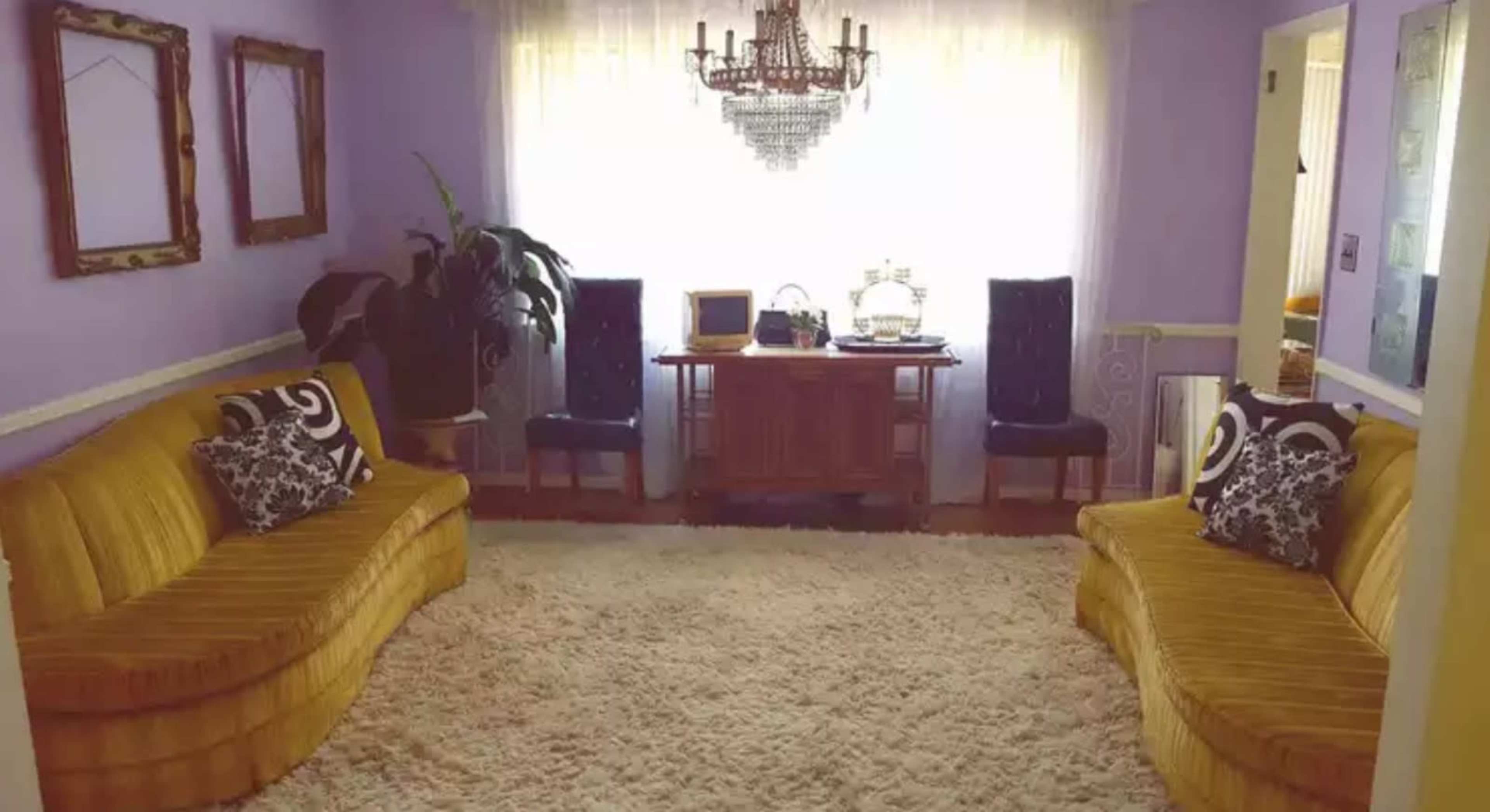 A living room features two yellow sofas, a large area rug, and a wooden table with decor under a chandelier.